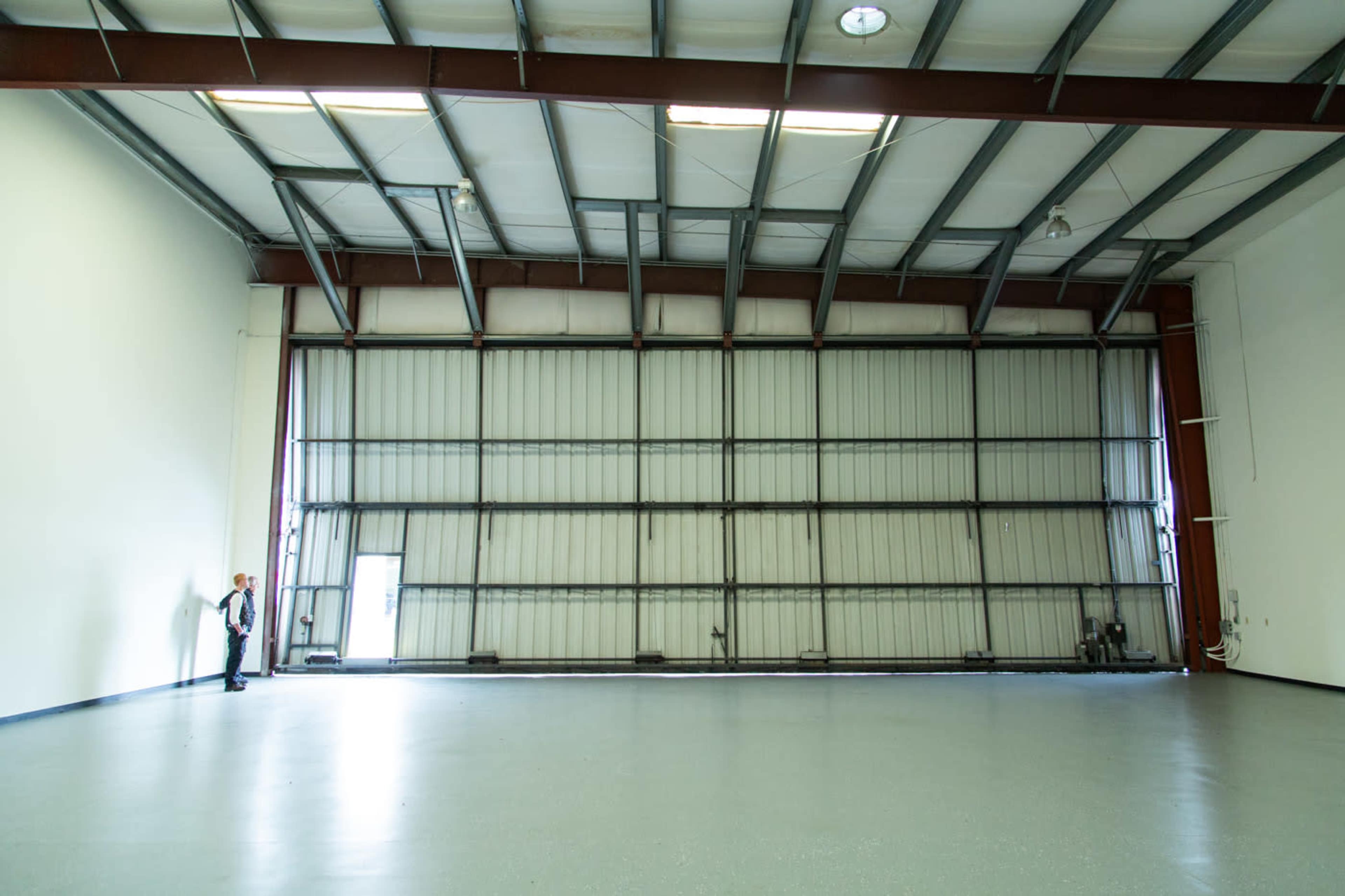 A large, empty industrial space with a high ceiling and a partially open sliding door on one side.