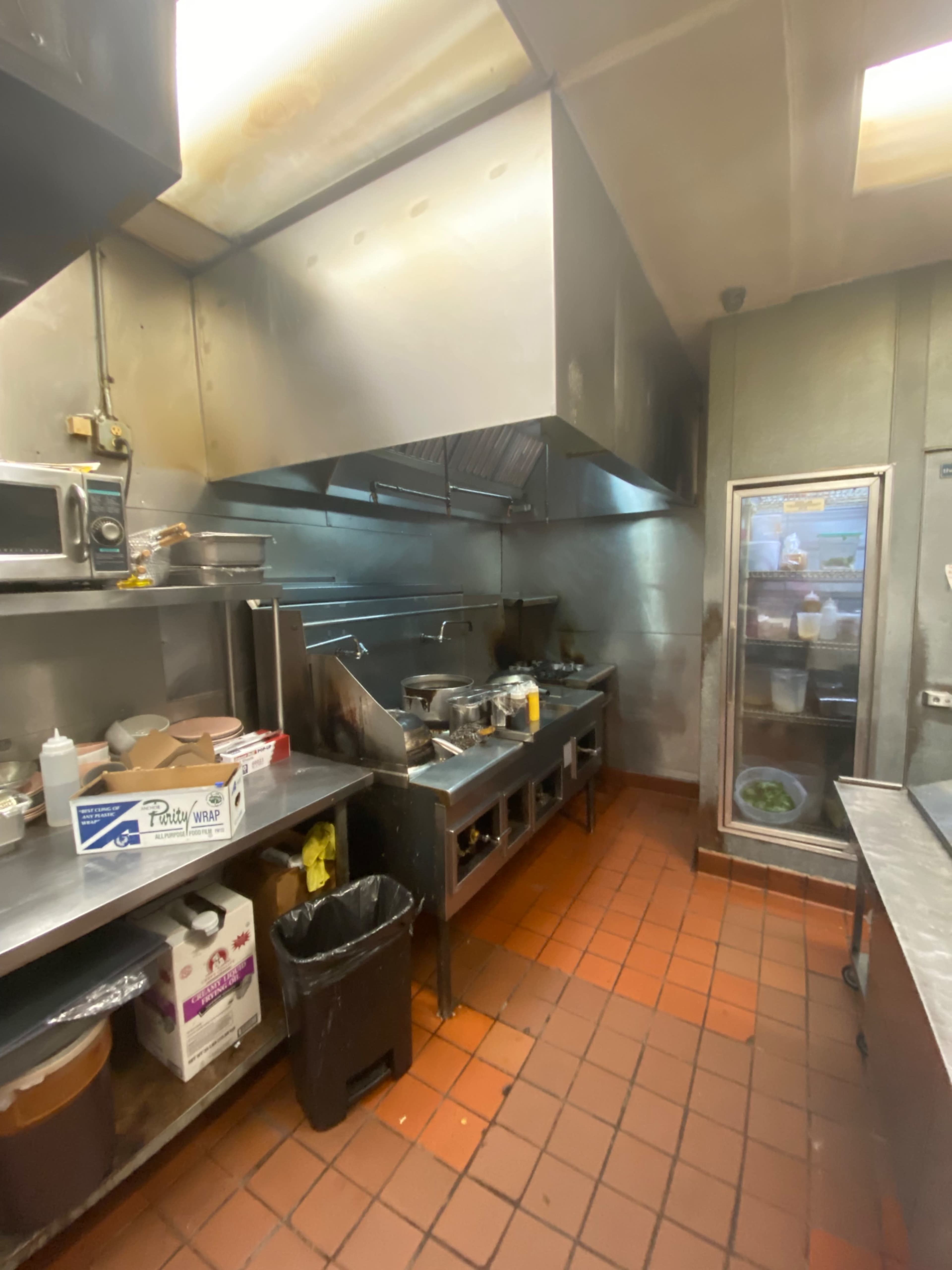 A commercial kitchen with stainless steel appliances, a ventilation hood, and various cooking equipment along the walls.