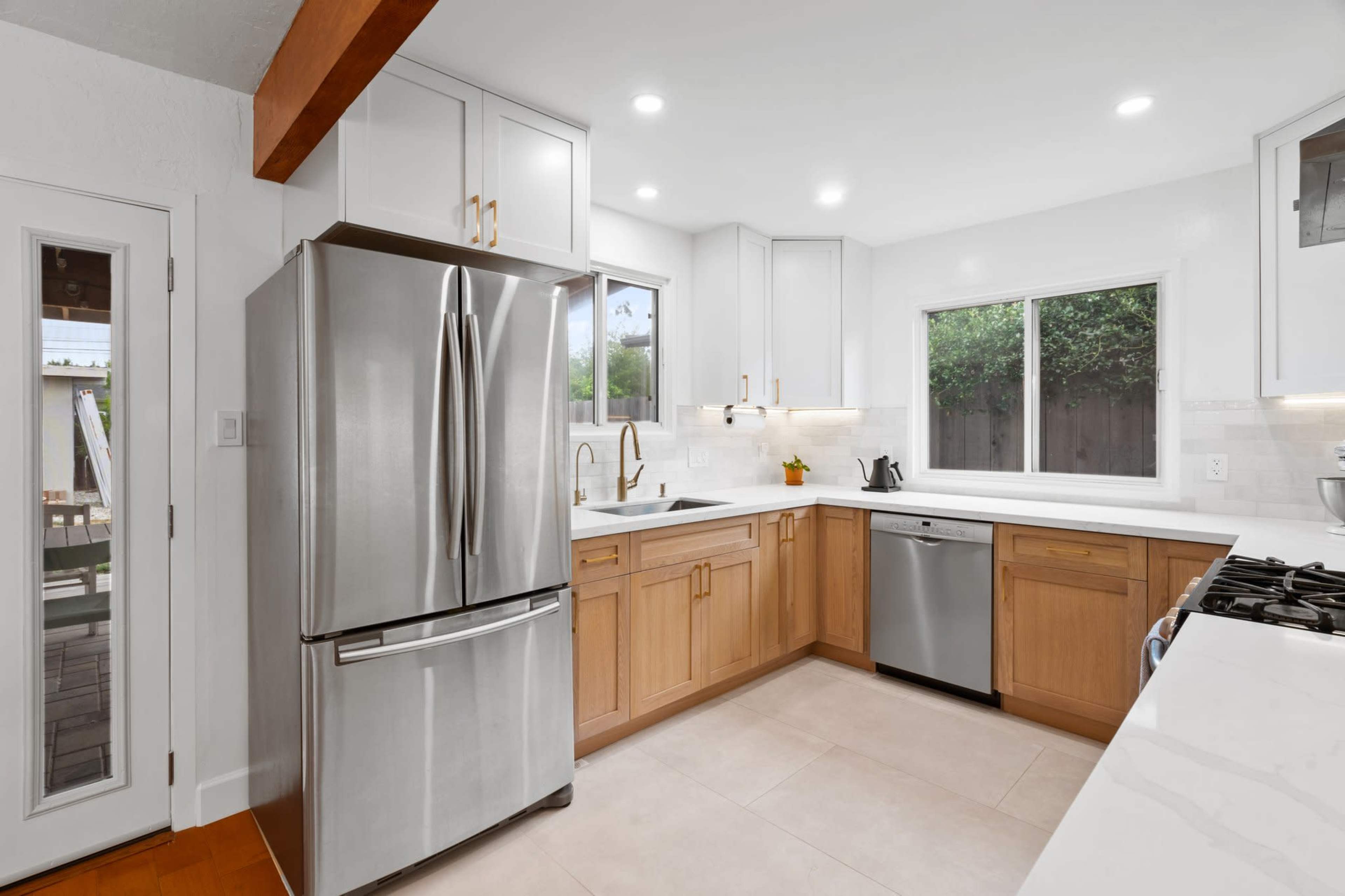 A modern kitchen featuring stainless steel appliances, wooden cabinets, and white countertops with a large window for natural light.