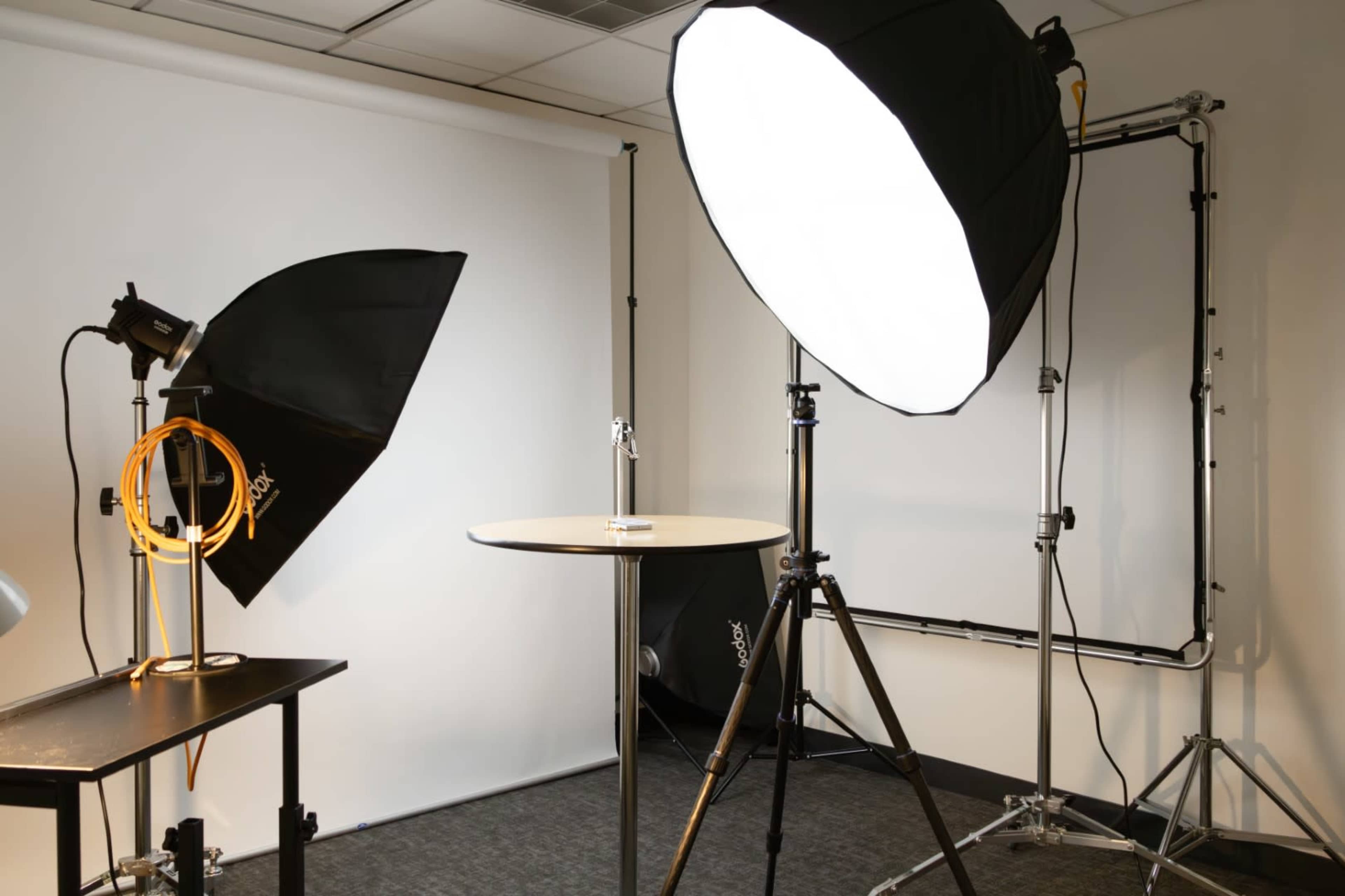 A photography studio setup with two lighting softboxes, a circular table, and a backdrop.