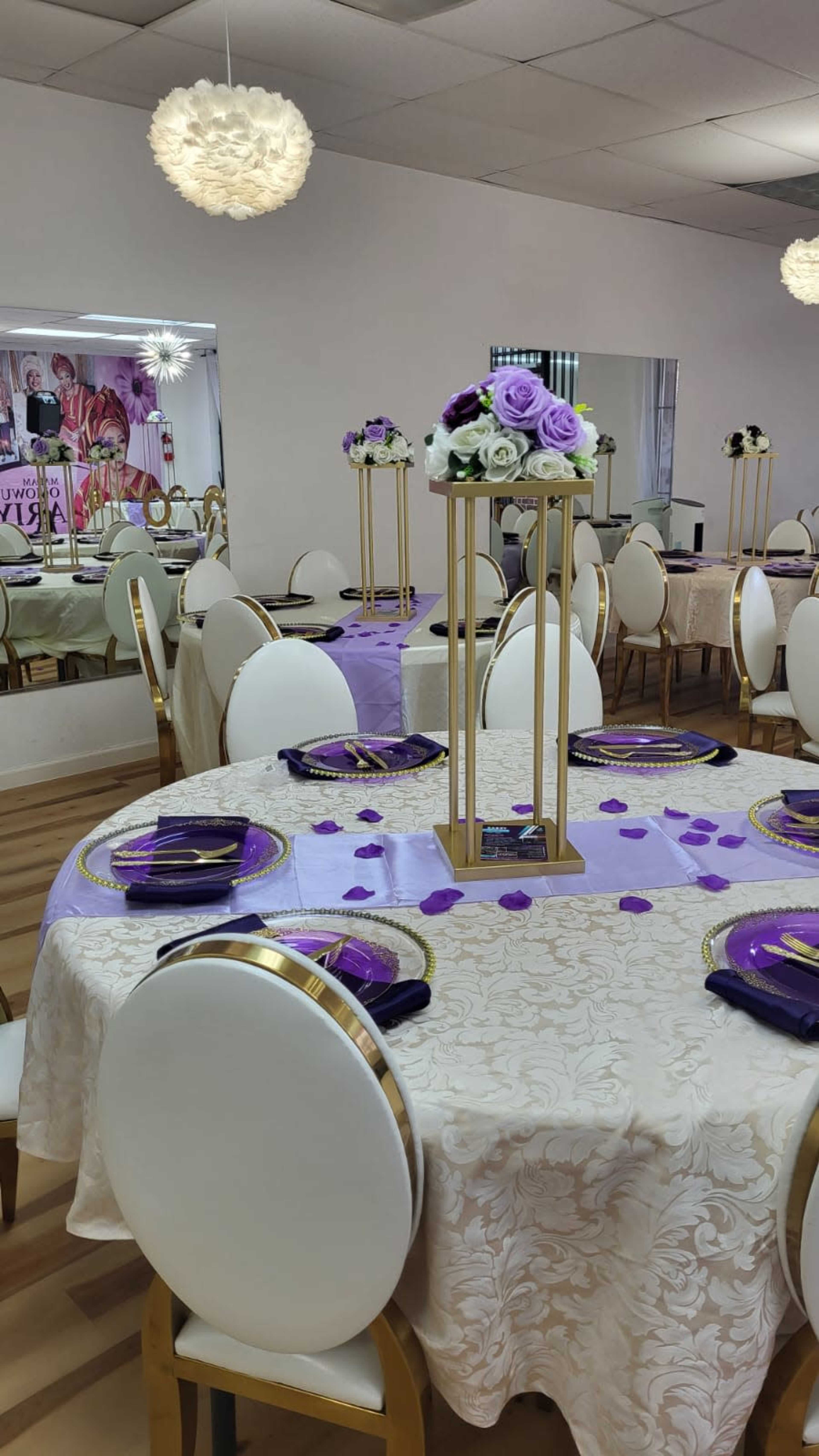 A banquet hall set up for an event, featuring round tables with elegant decorations, purple tablecloths, and floral centerpieces.