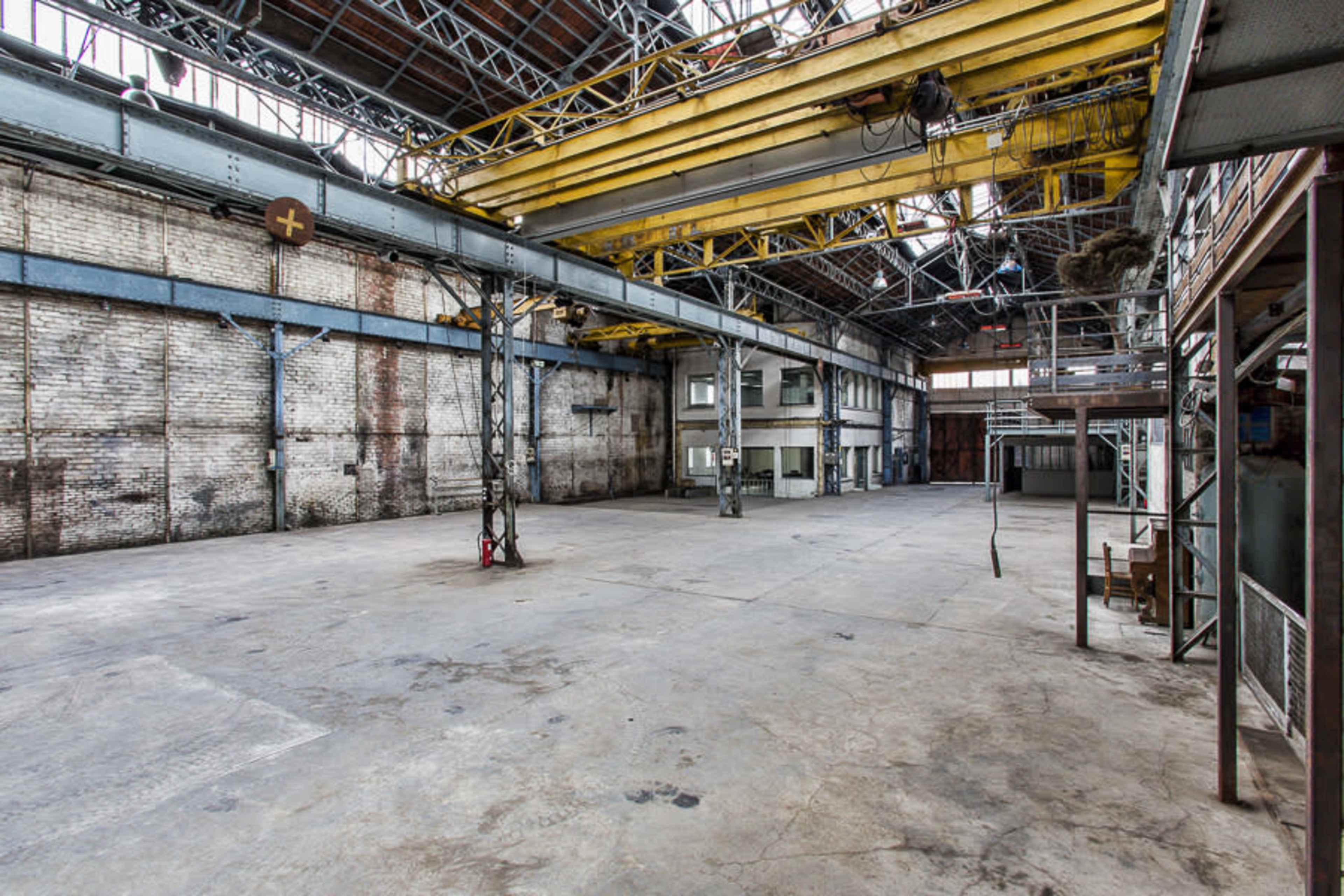 A large, empty industrial warehouse with exposed brick walls and high ceilings supported by metal beams.