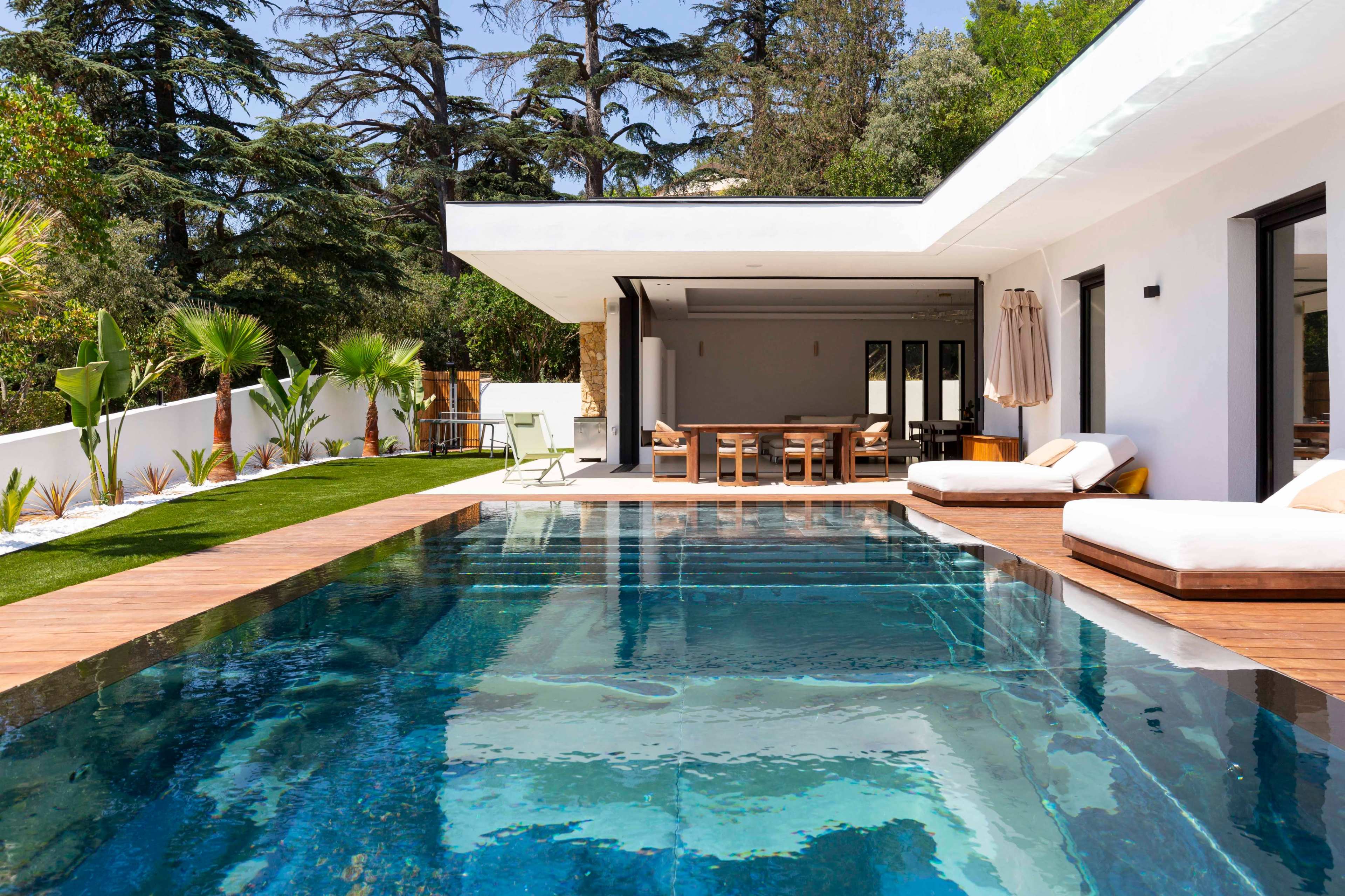 The image shows a modern villa with a swimming pool, surrounded by greenery and outdoor seating.
