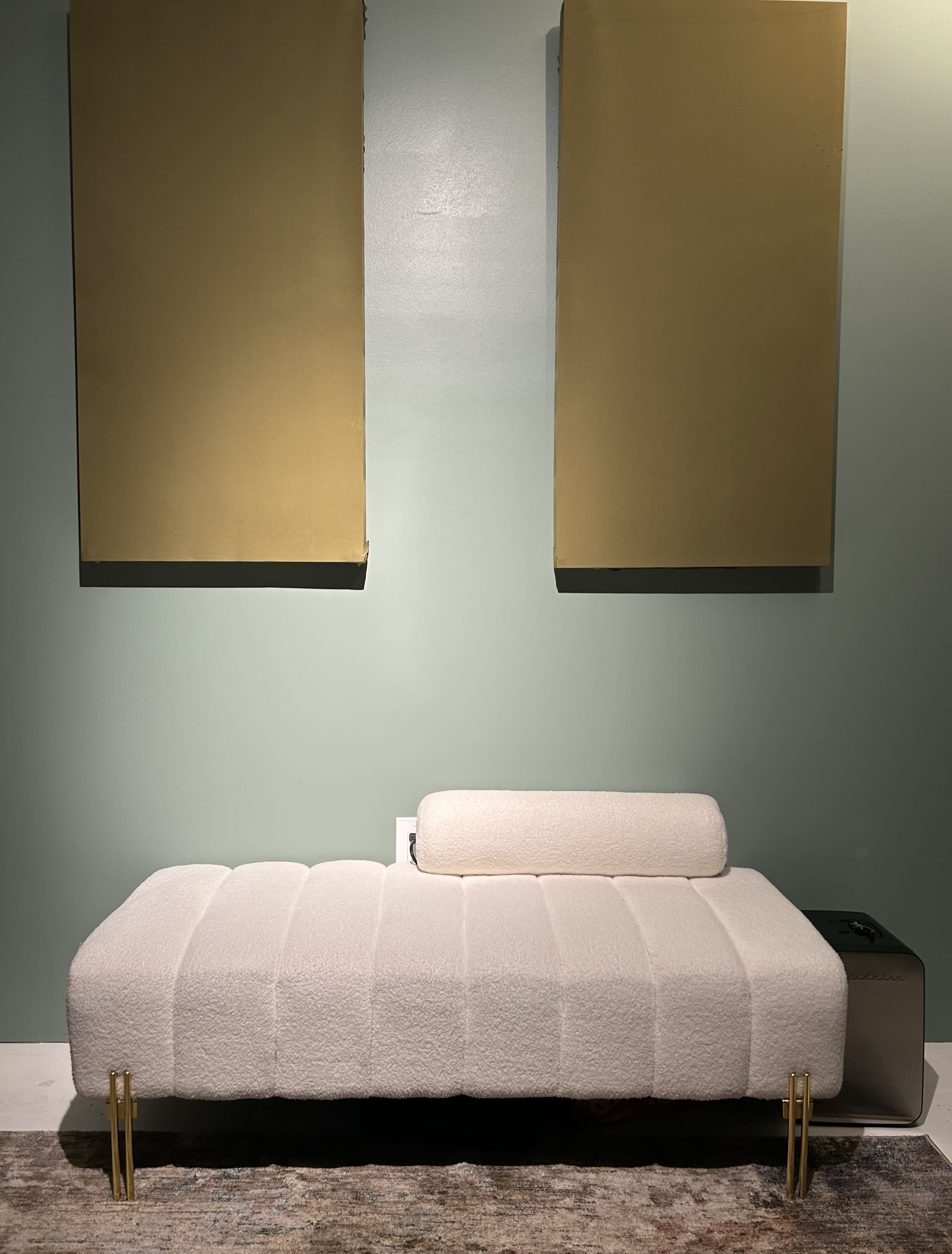 A white, textured sofa with gold legs is positioned against a green wall, flanked by two gold panels.