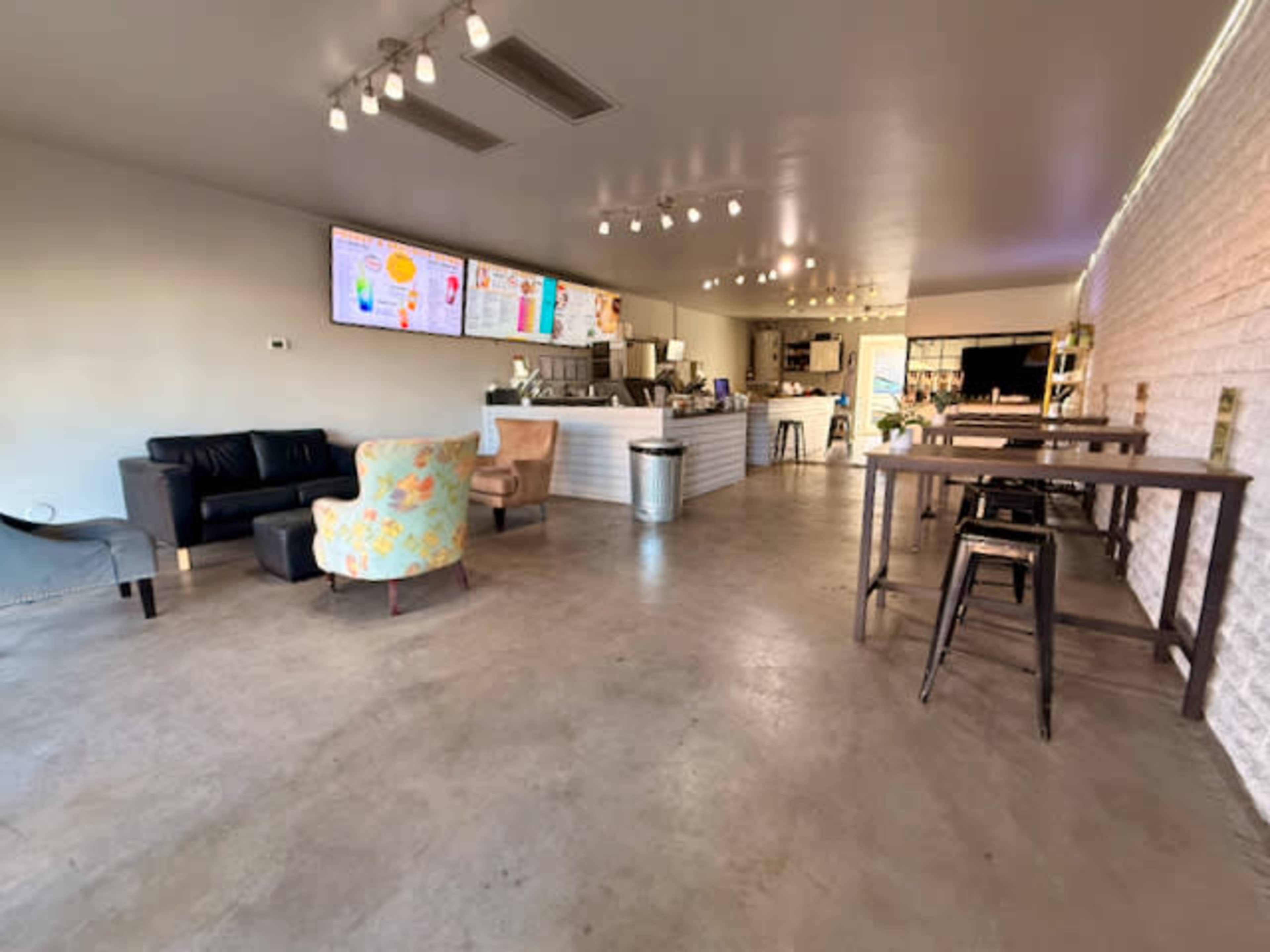 The image shows a modern café interior with a coffee counter, seating areas, and large screens displaying menus.