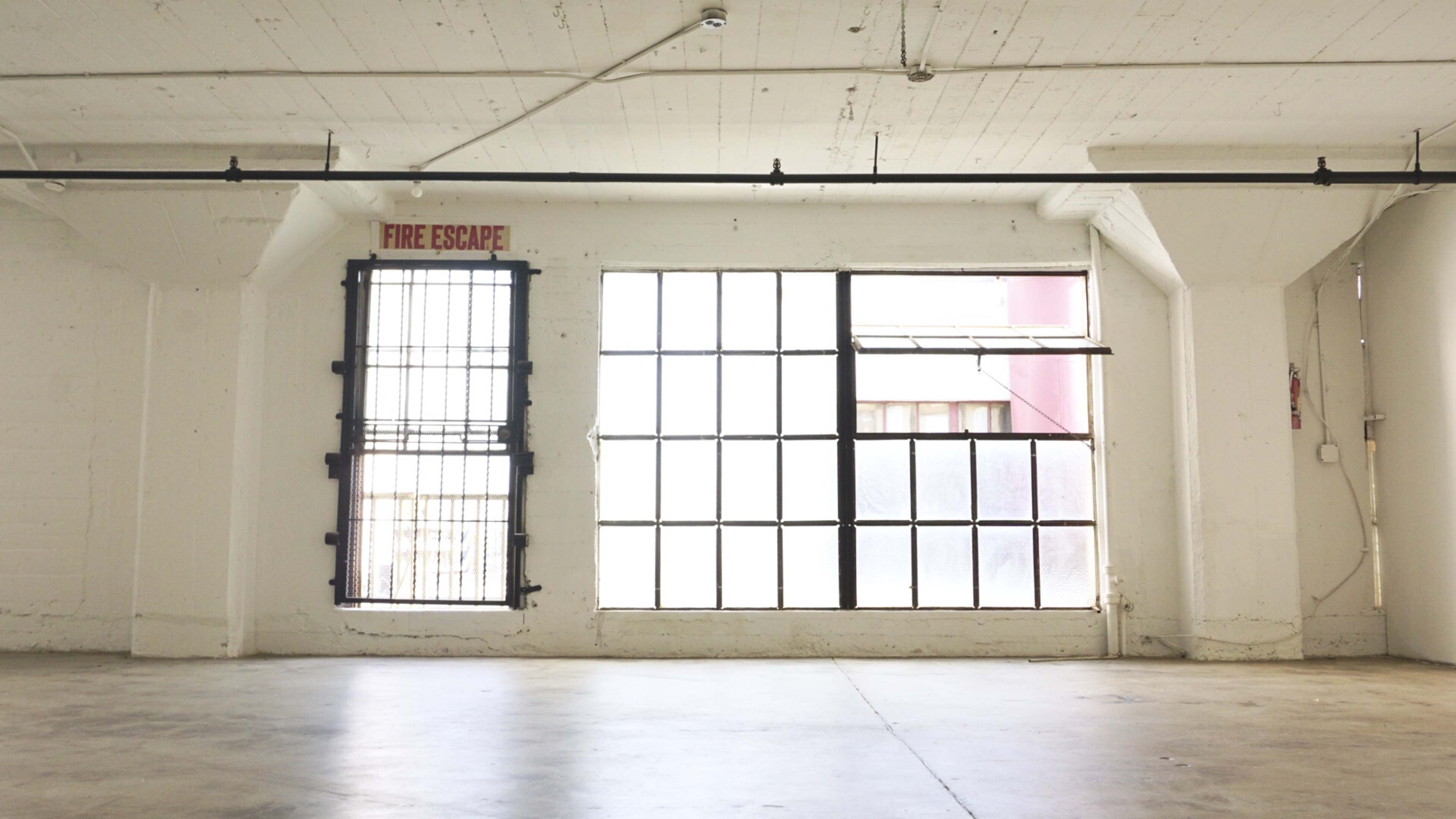 The image shows a spacious, empty room with large windows and a fire escape sign mounted above.