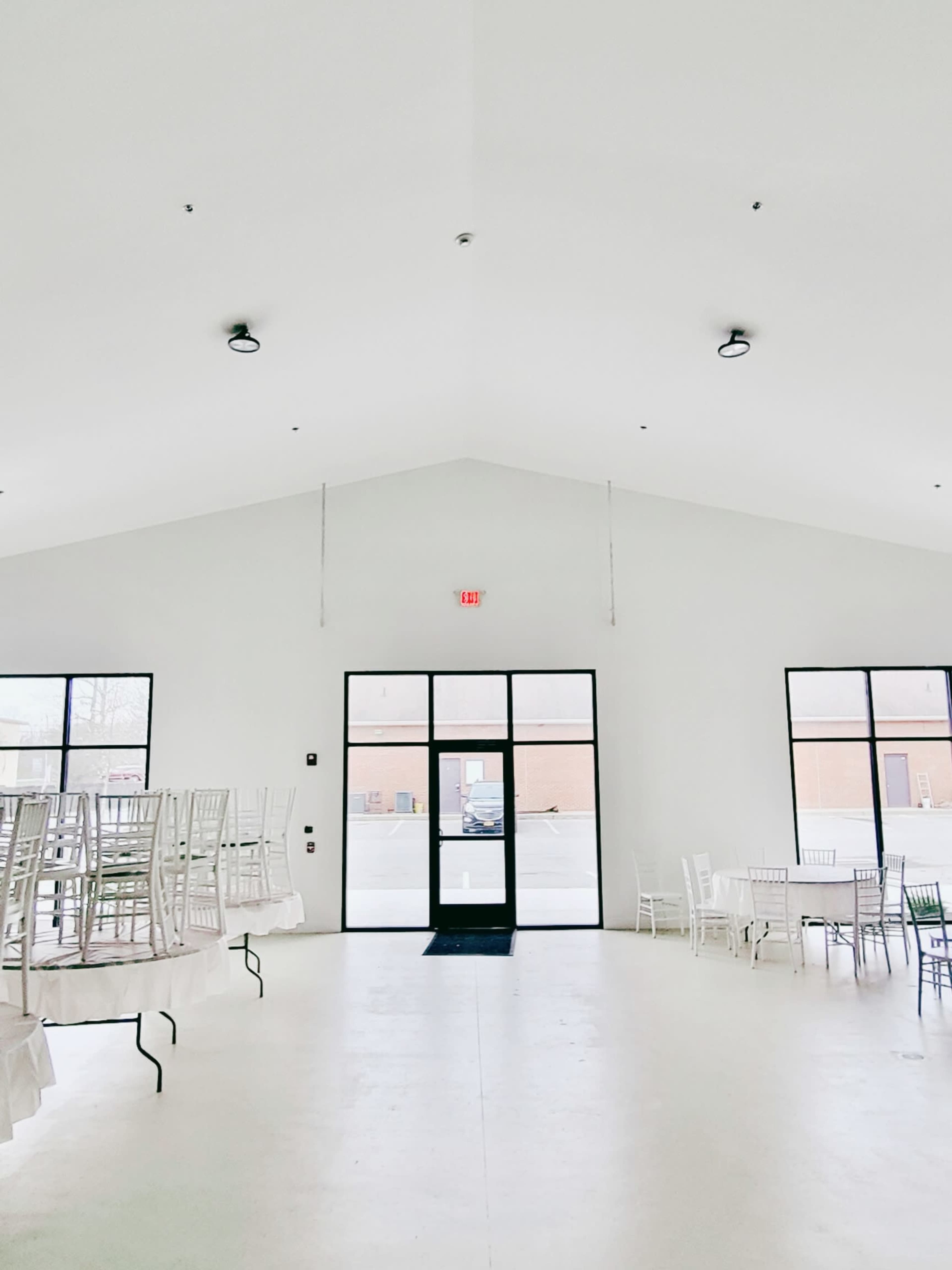 A spacious, empty room with white walls, tall ceilings, and several stacked chairs arranged around the perimeter.
