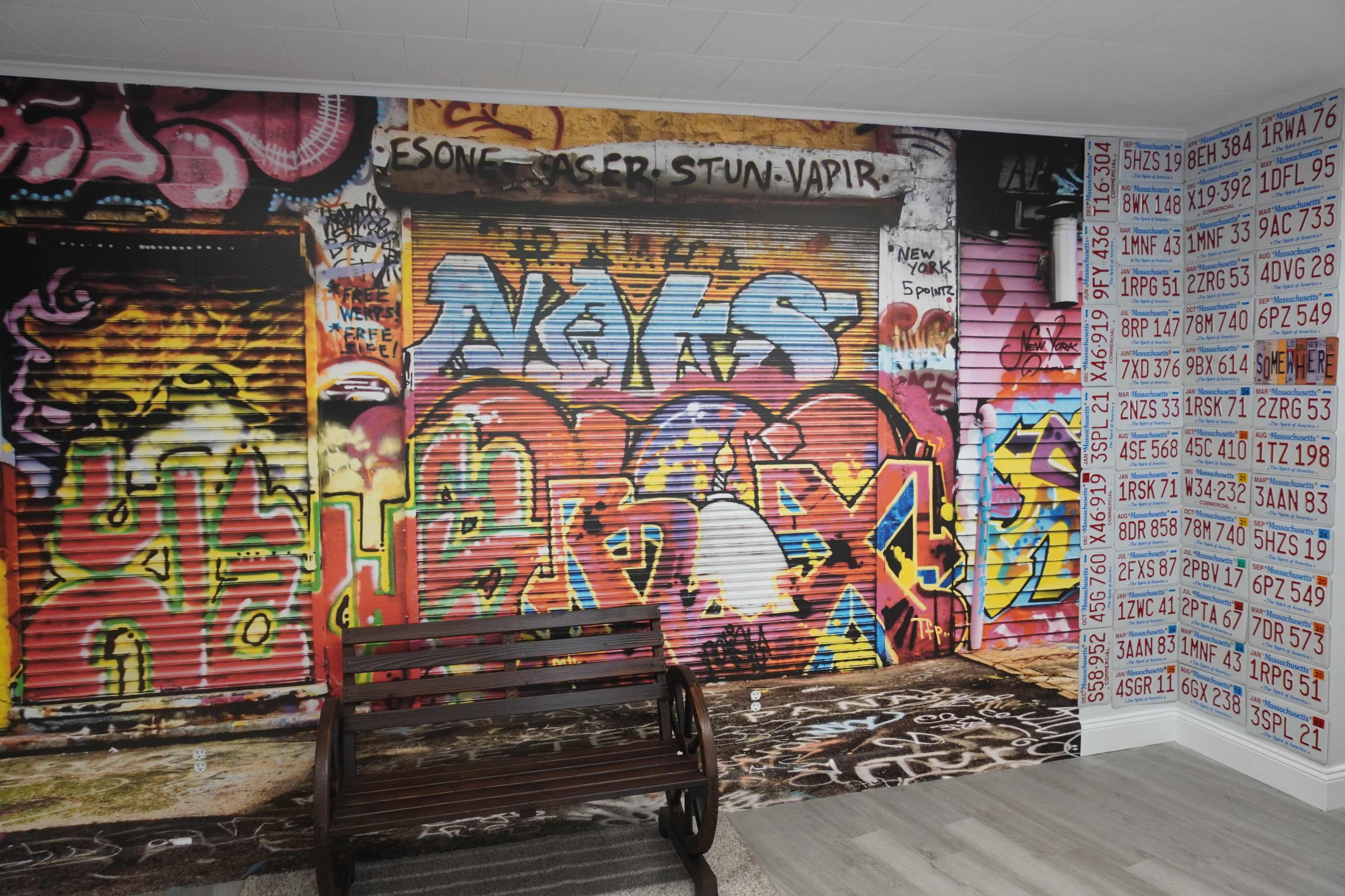 A wall covered in vibrant graffiti art alongside a wooden bench placed on a patterned floor.