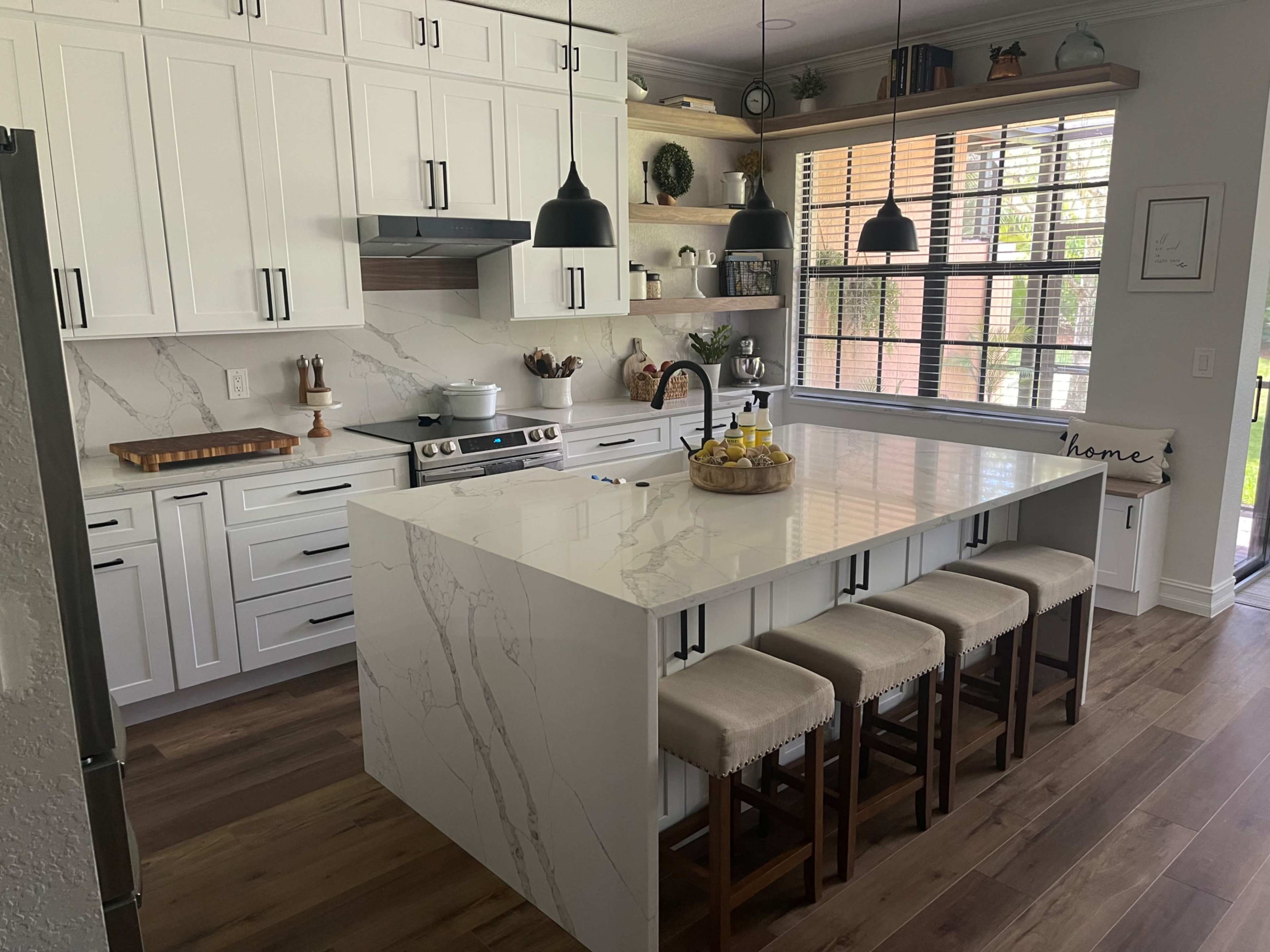 A modern kitchen featuring white cabinetry, a large island with a marble countertop, and four wooden stools.
