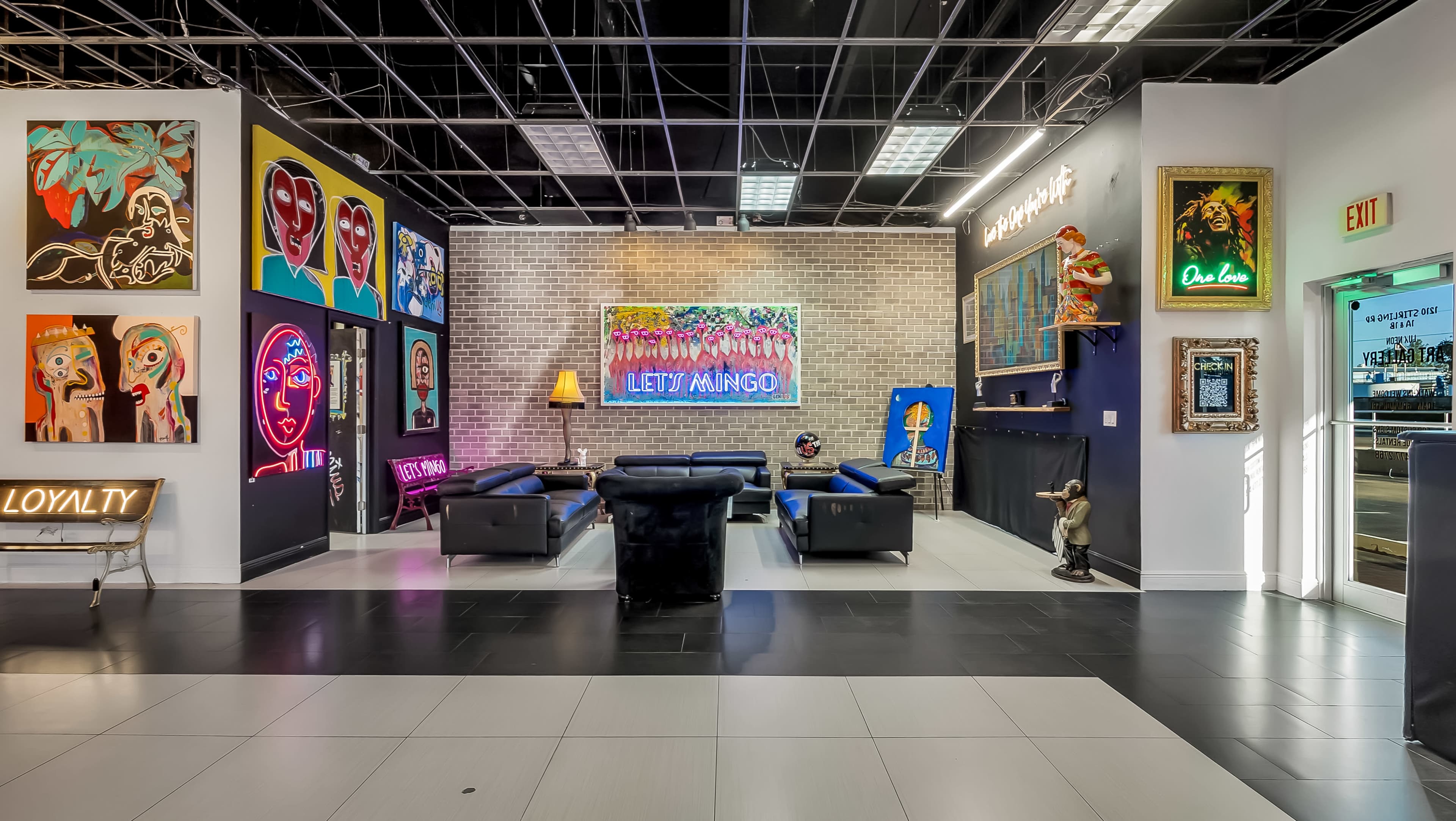The image depicts a modern interior space featuring colorful artwork on the walls, a seating area with black couches, and vibrant neon signs.