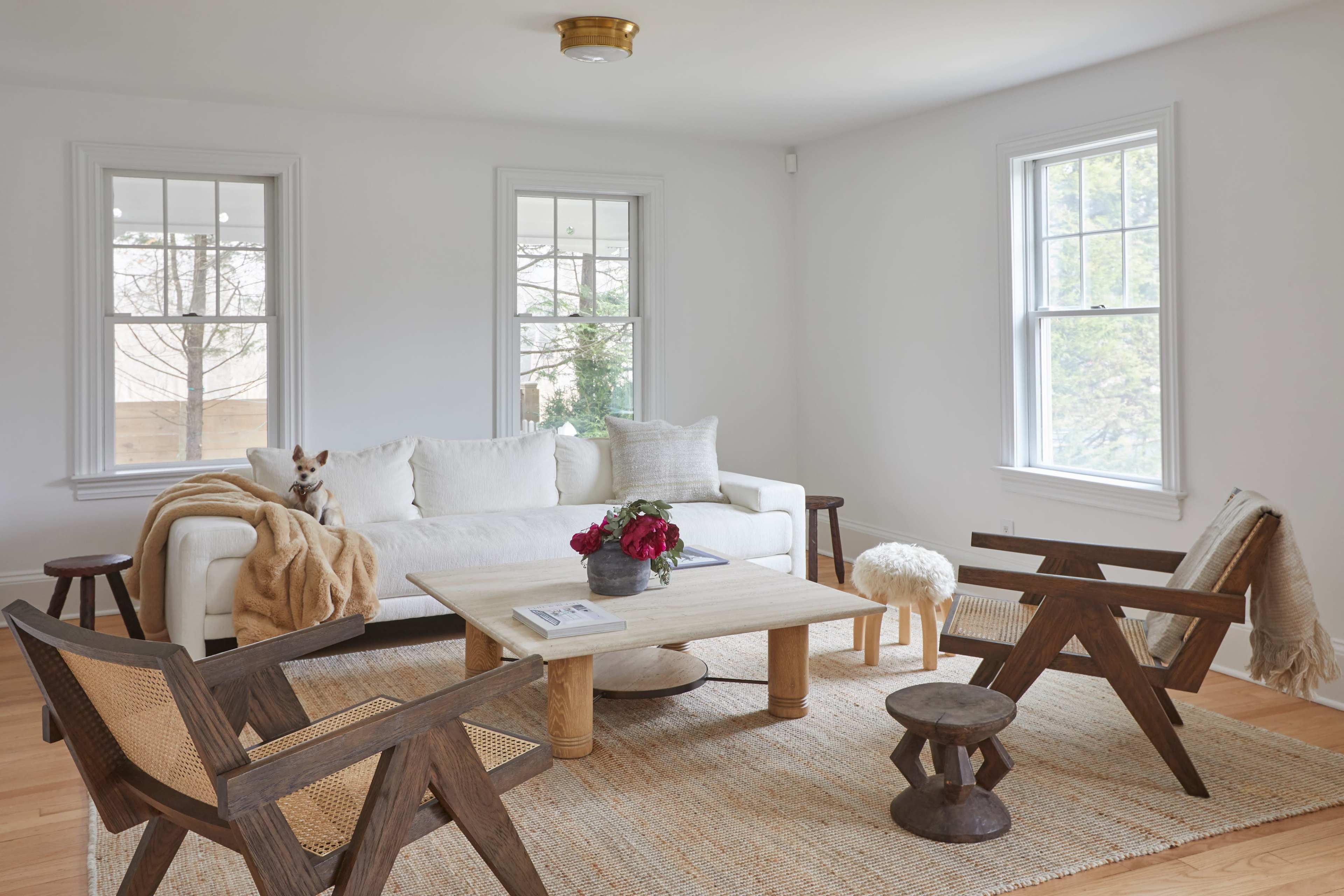 A bright living room with a white sofa, two wooden chairs, a round coffee table, and a woven rug.