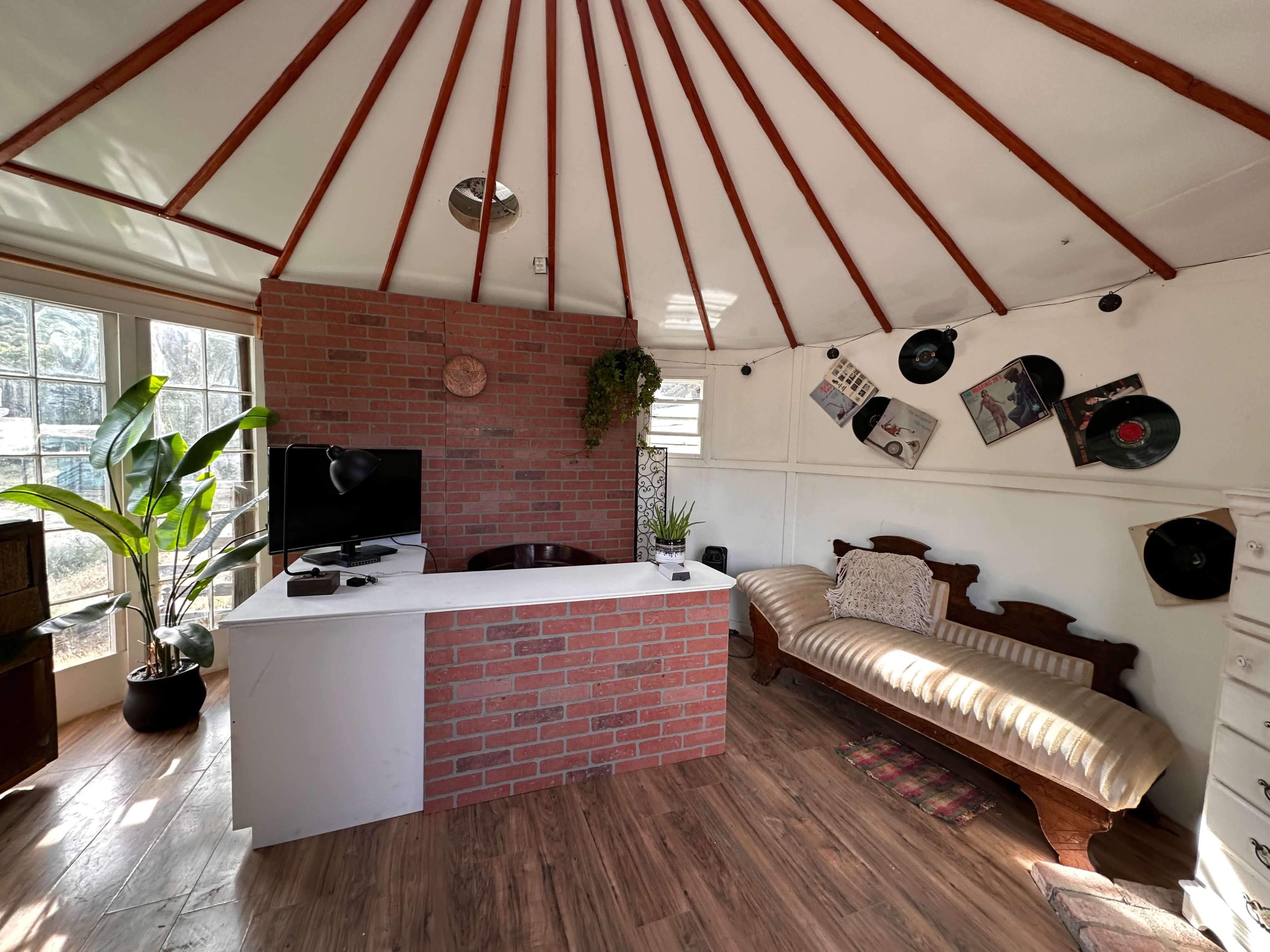 The image shows a small interior space with a brick-patterned counter, a television, a couch along the wall, and decorative vinyl records hanging from the ceiling.