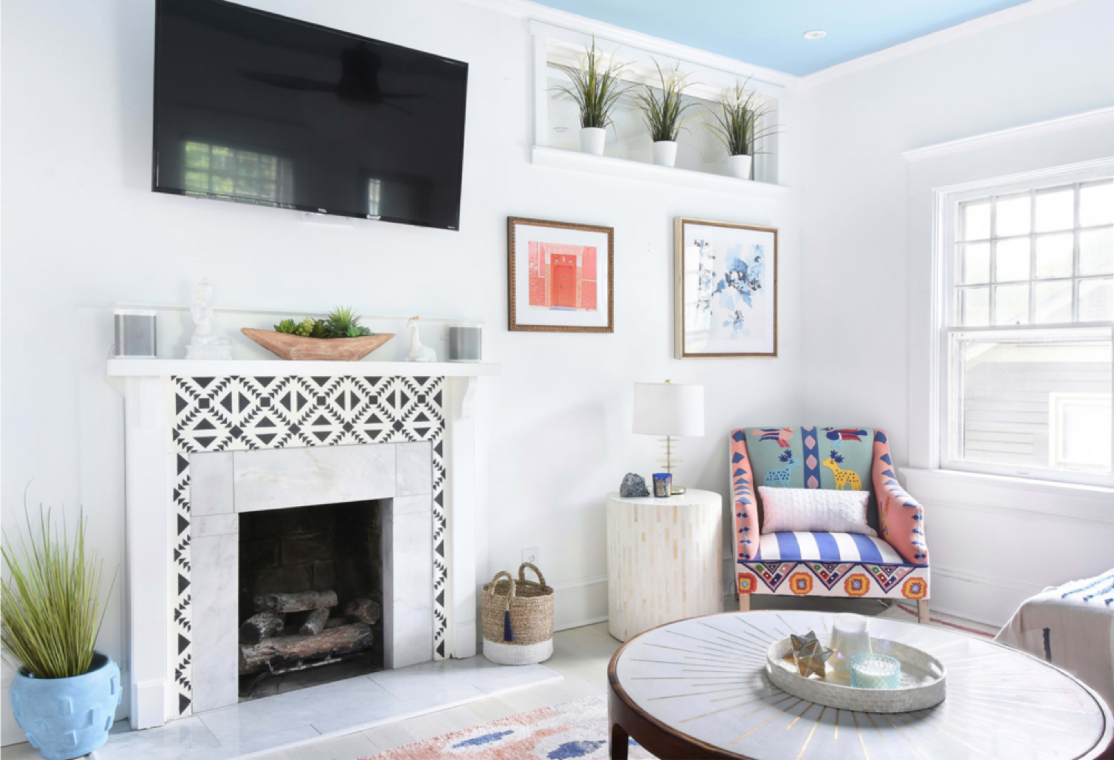 The living room features a patterned fireplace, a mounted television, and colorful artwork on the walls, along with a cozy armchair and a round coffee table.