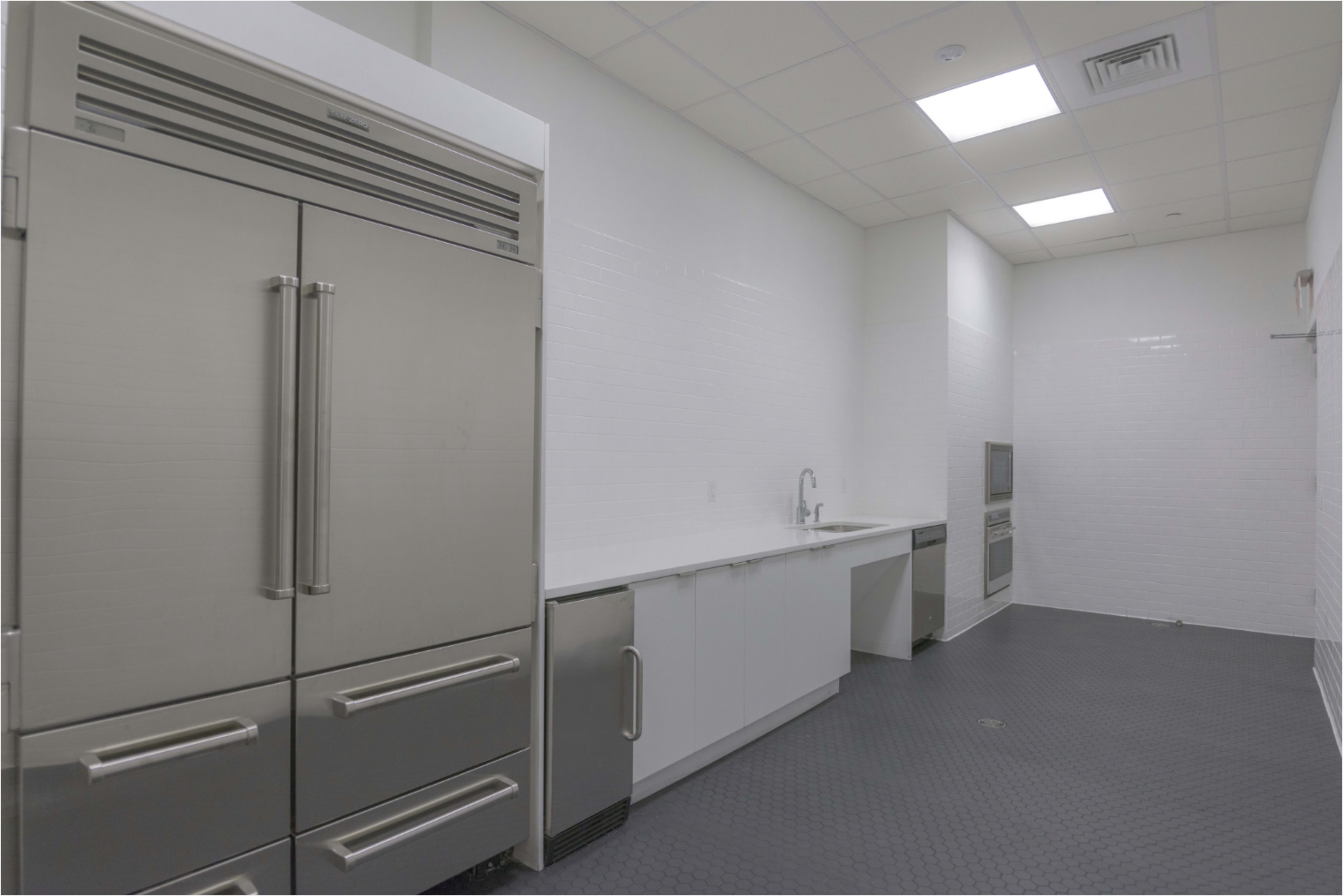 The image shows a modern kitchen with stainless steel appliances, including a large refrigerator, white countertops, and tiled walls.