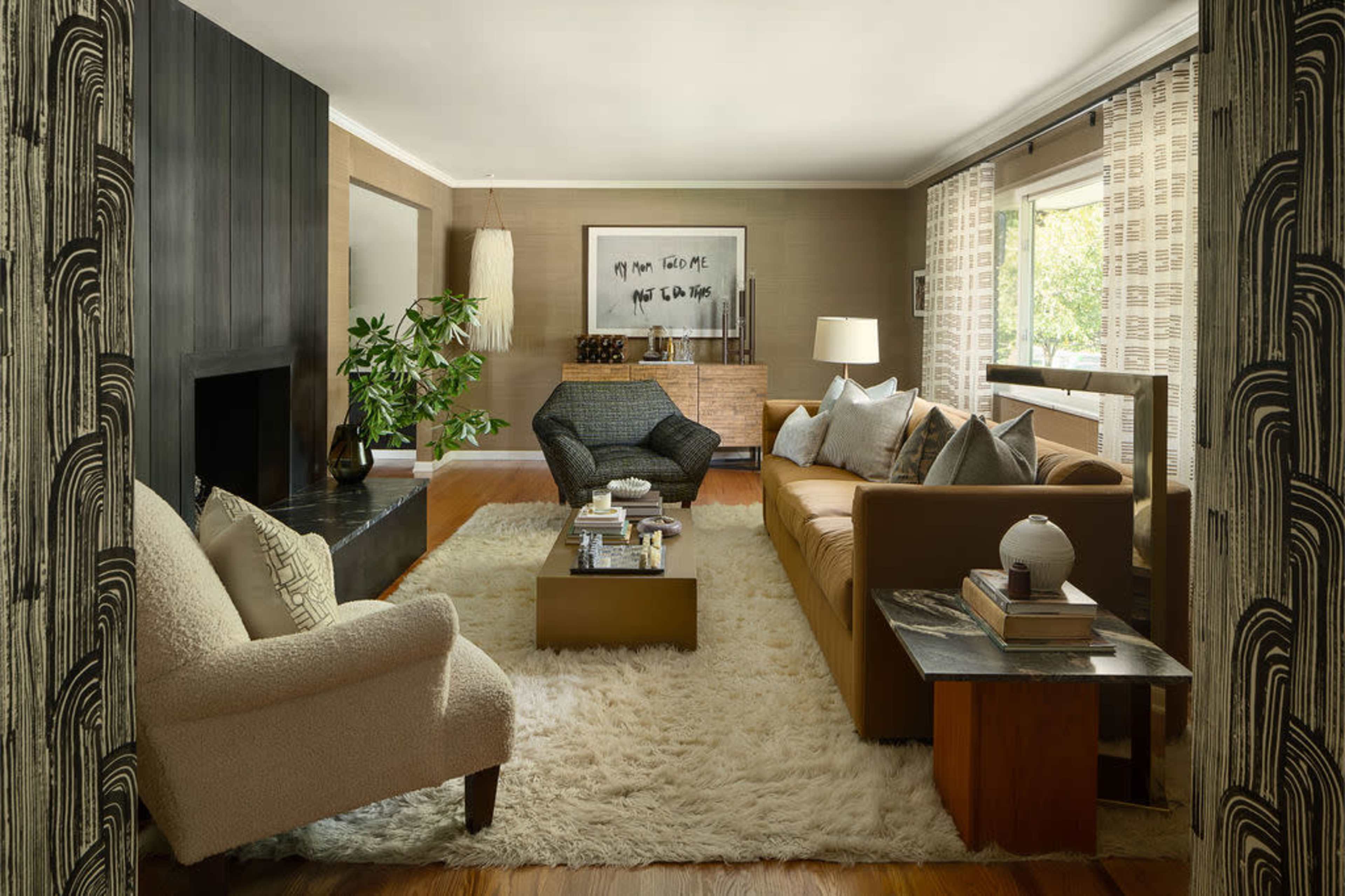 A modern living room featuring a brown leather sofa, a patterned armchair, a coffee table with books, and a large rug on a hardwood floor.