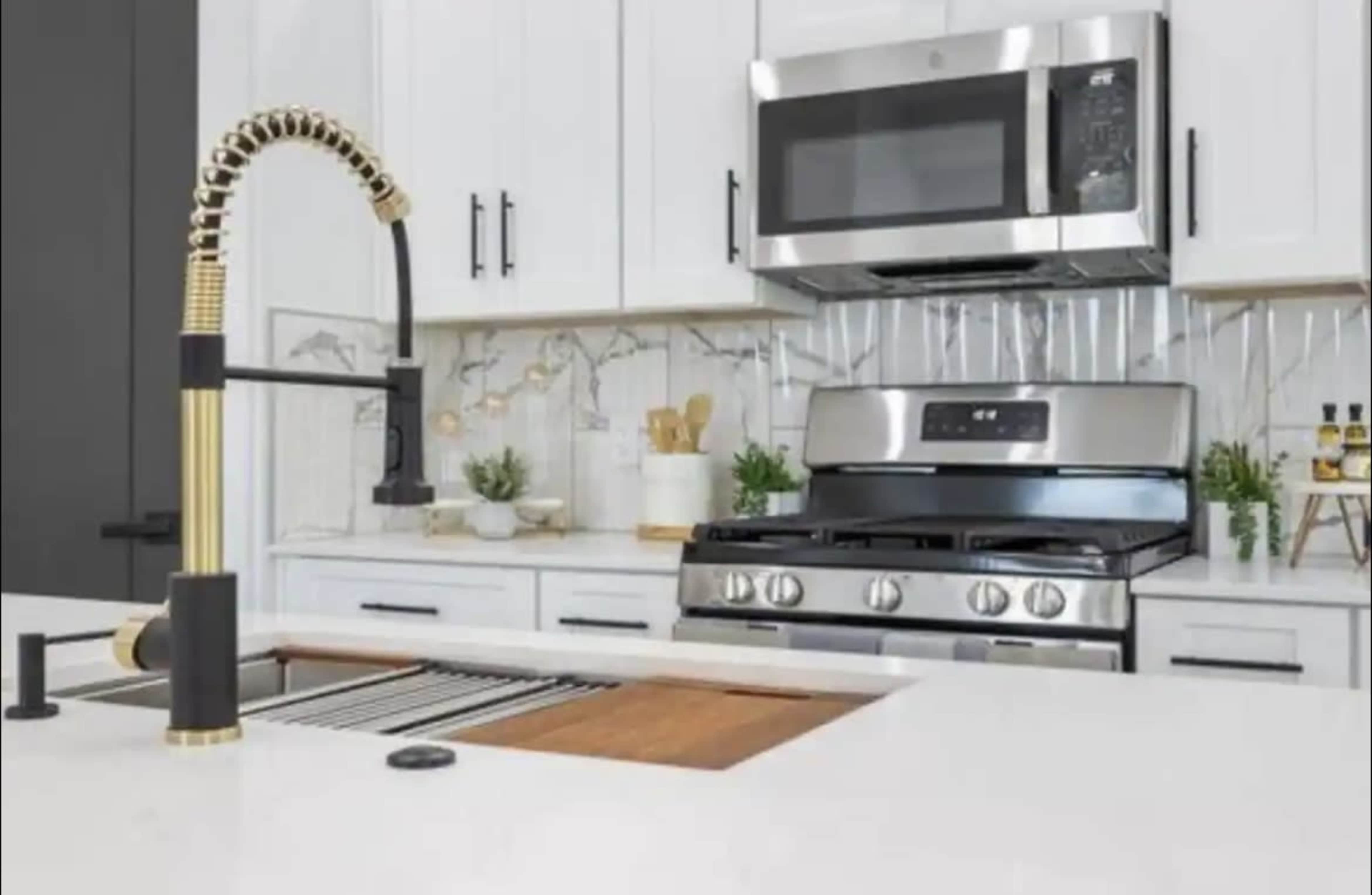 A modern kitchen featuring a stainless steel stove and microwave, a sleek sink with a gold faucet, and white cabinetry with decorative accents.