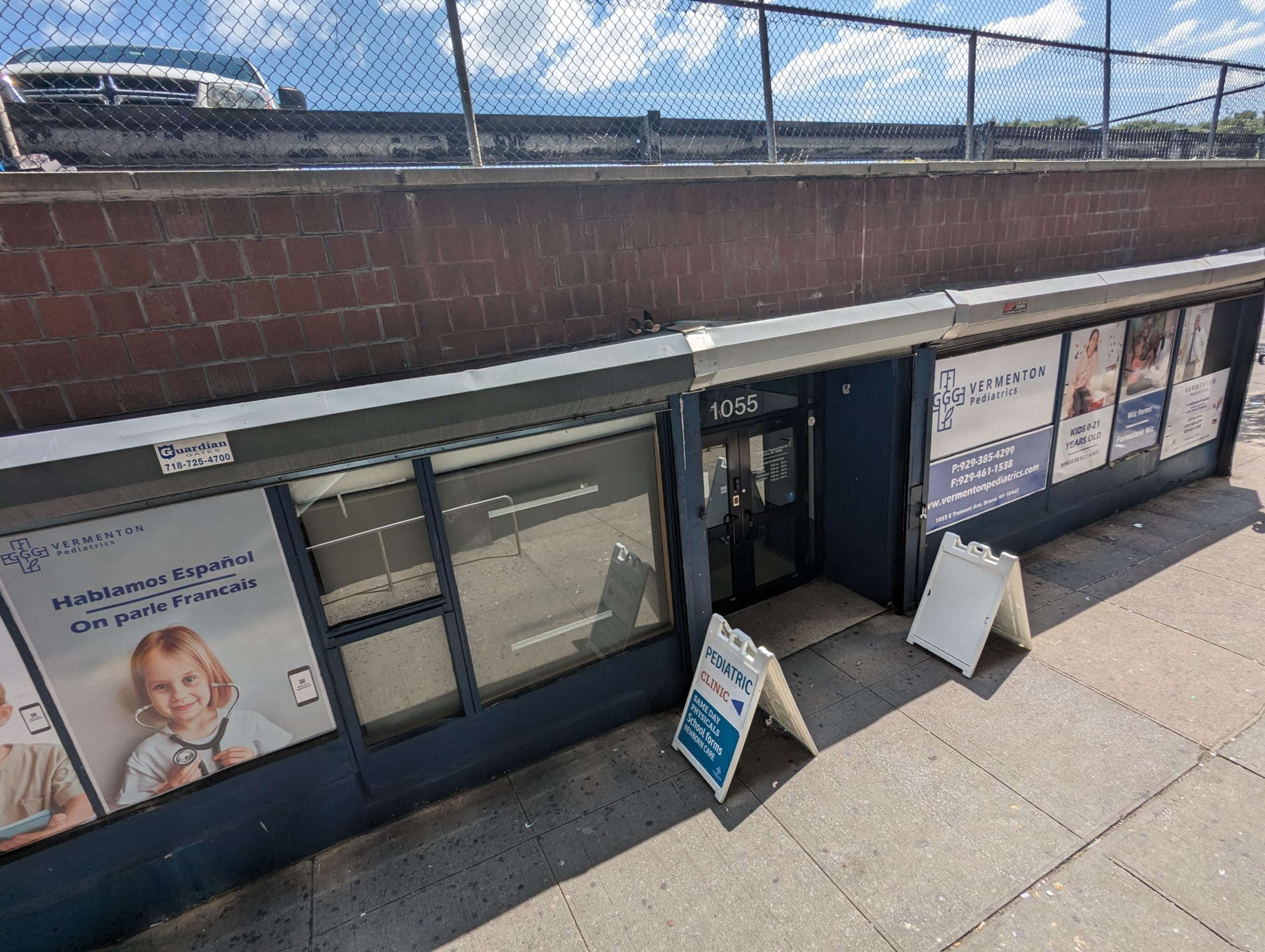 A storefront with signs indicating services in Spanish and French, located at 1055, beneath a fence on a sunny day.