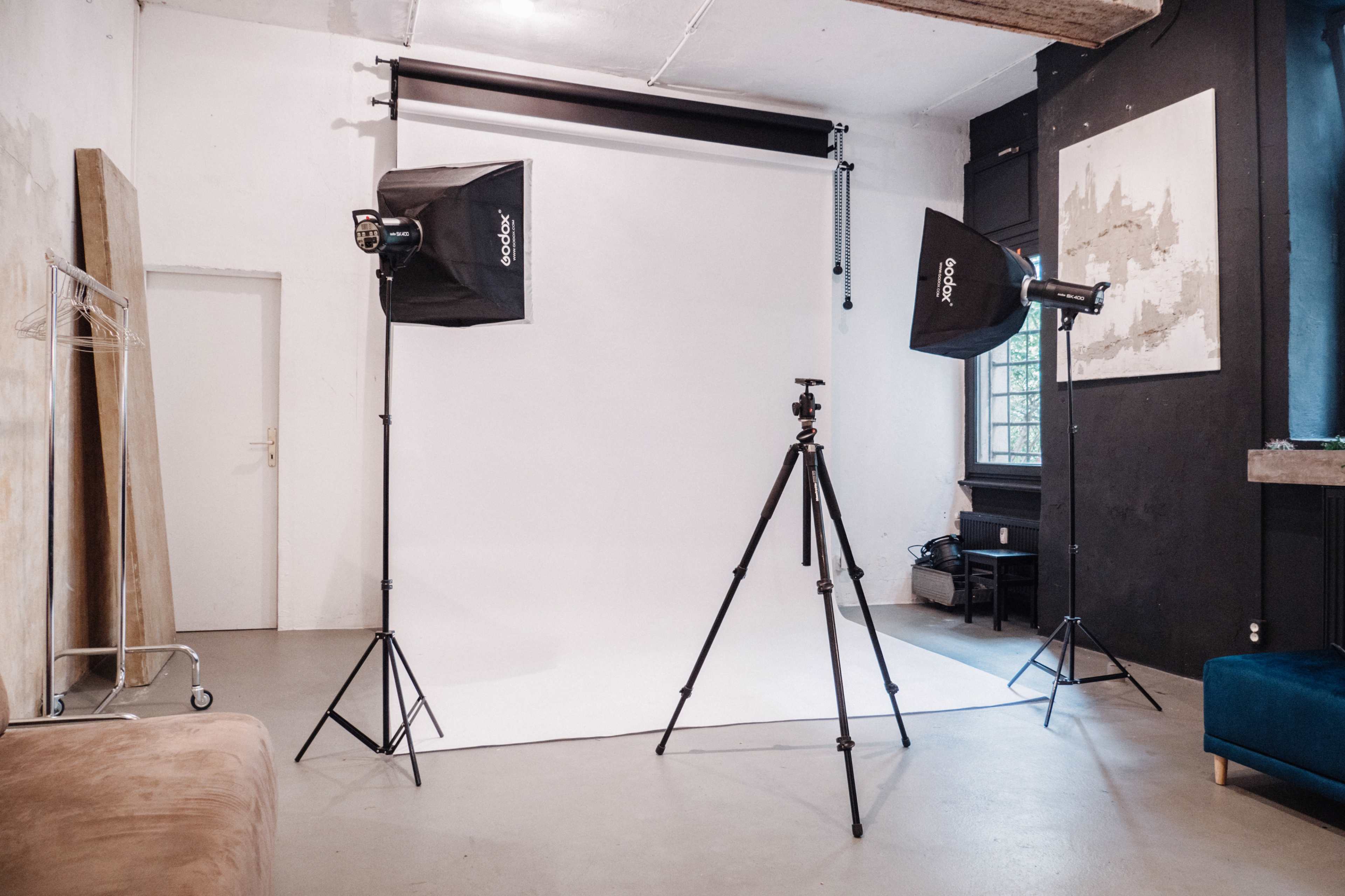 A photography studio setup with two softbox lights, a camera tripod, and a white backdrop in a minimalistic room.