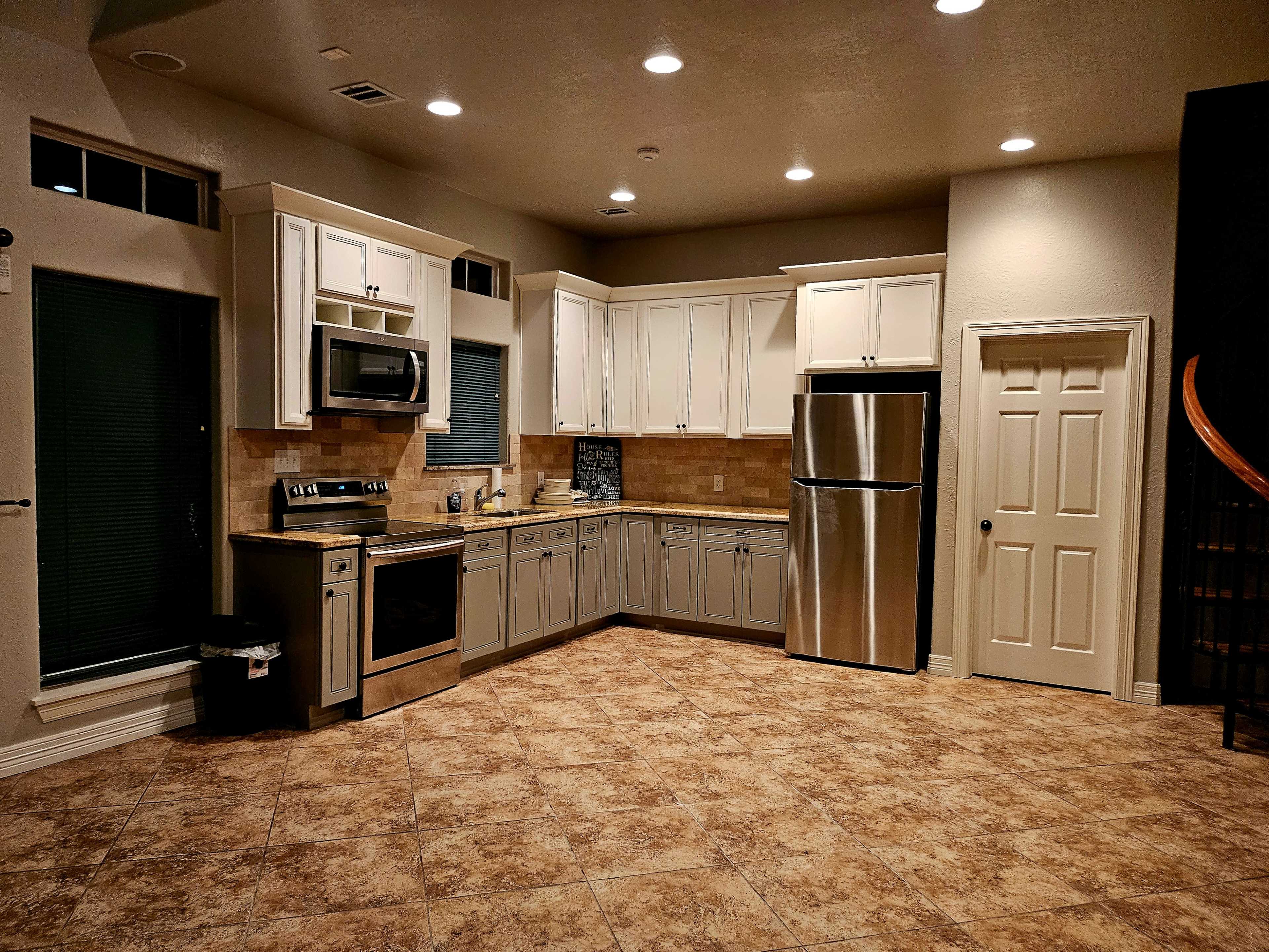 The image shows a modern kitchen with stainless steel appliances, light-colored cabinetry, and tiled flooring.