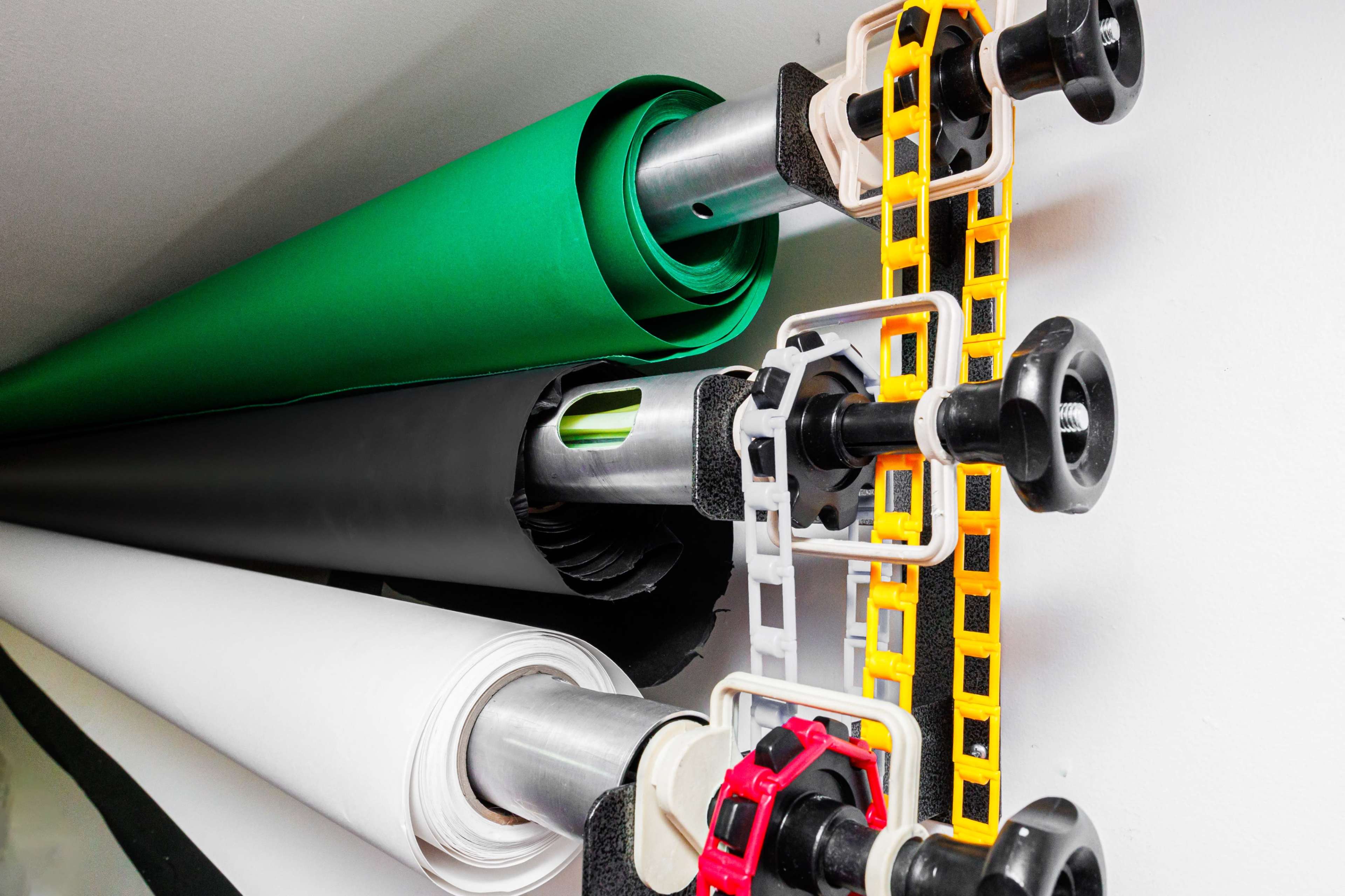Rolls of colored paper organized on a rack, with green, black, and white rolls visible.