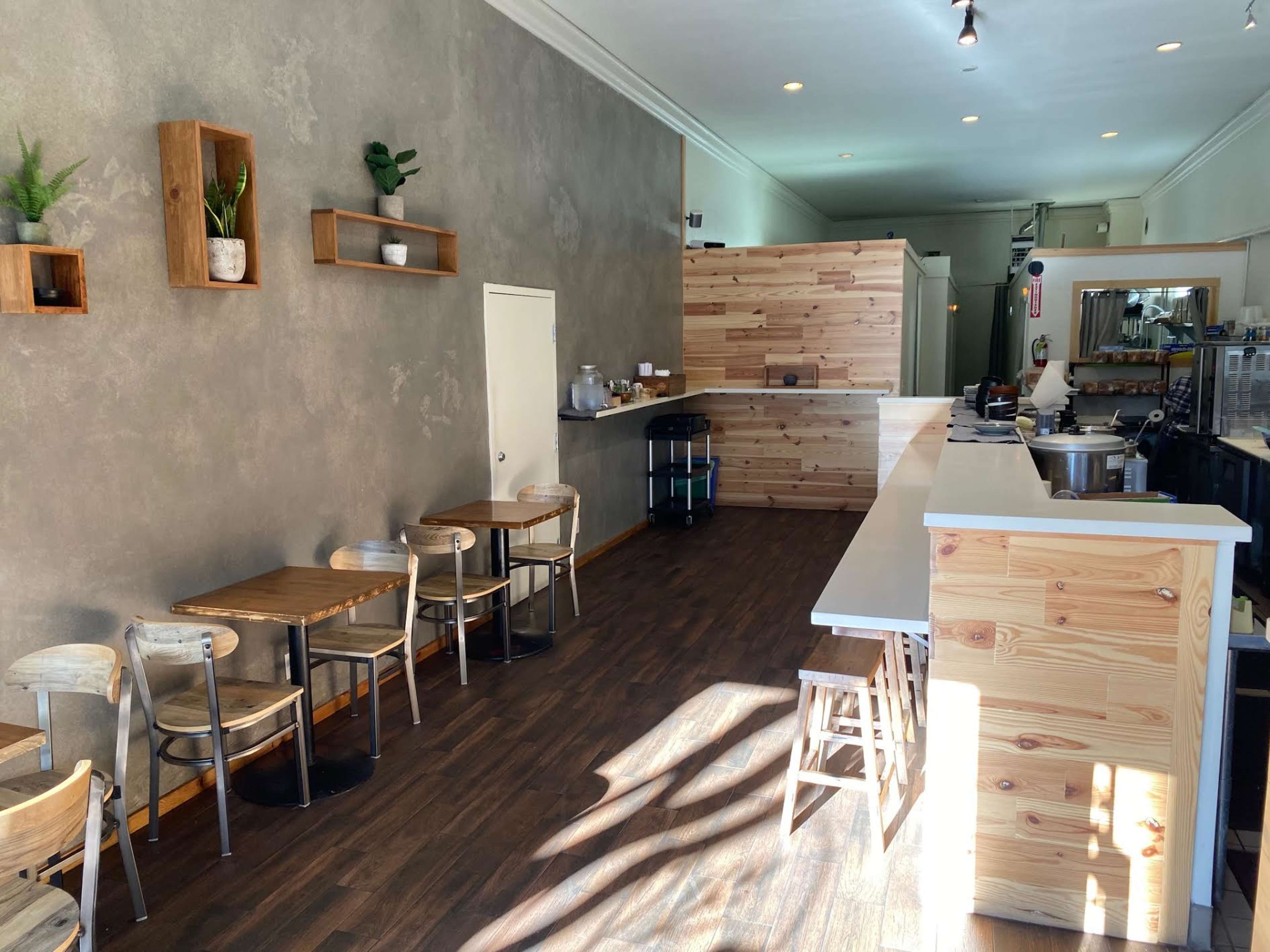 A minimalist café interior with wooden furniture, a simple counter, and a few potted plants on the walls.