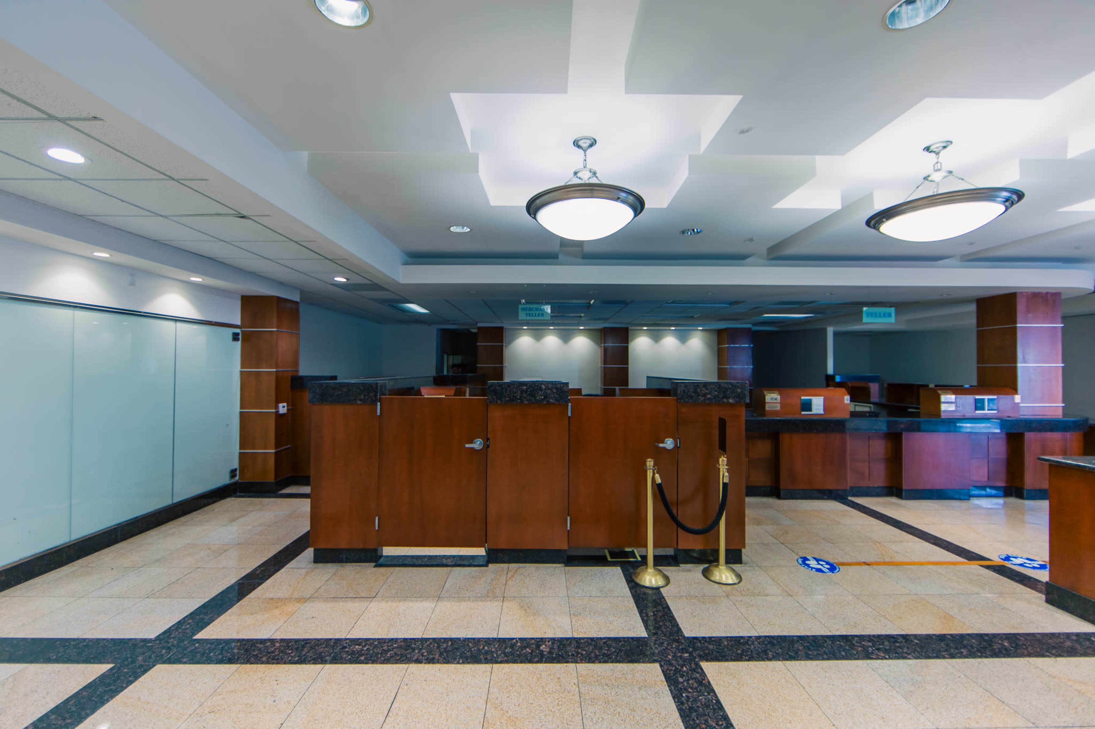 The image shows an empty bank interior with wooden service counters and a tiled floor, featuring a stanchion and signs on the ground.