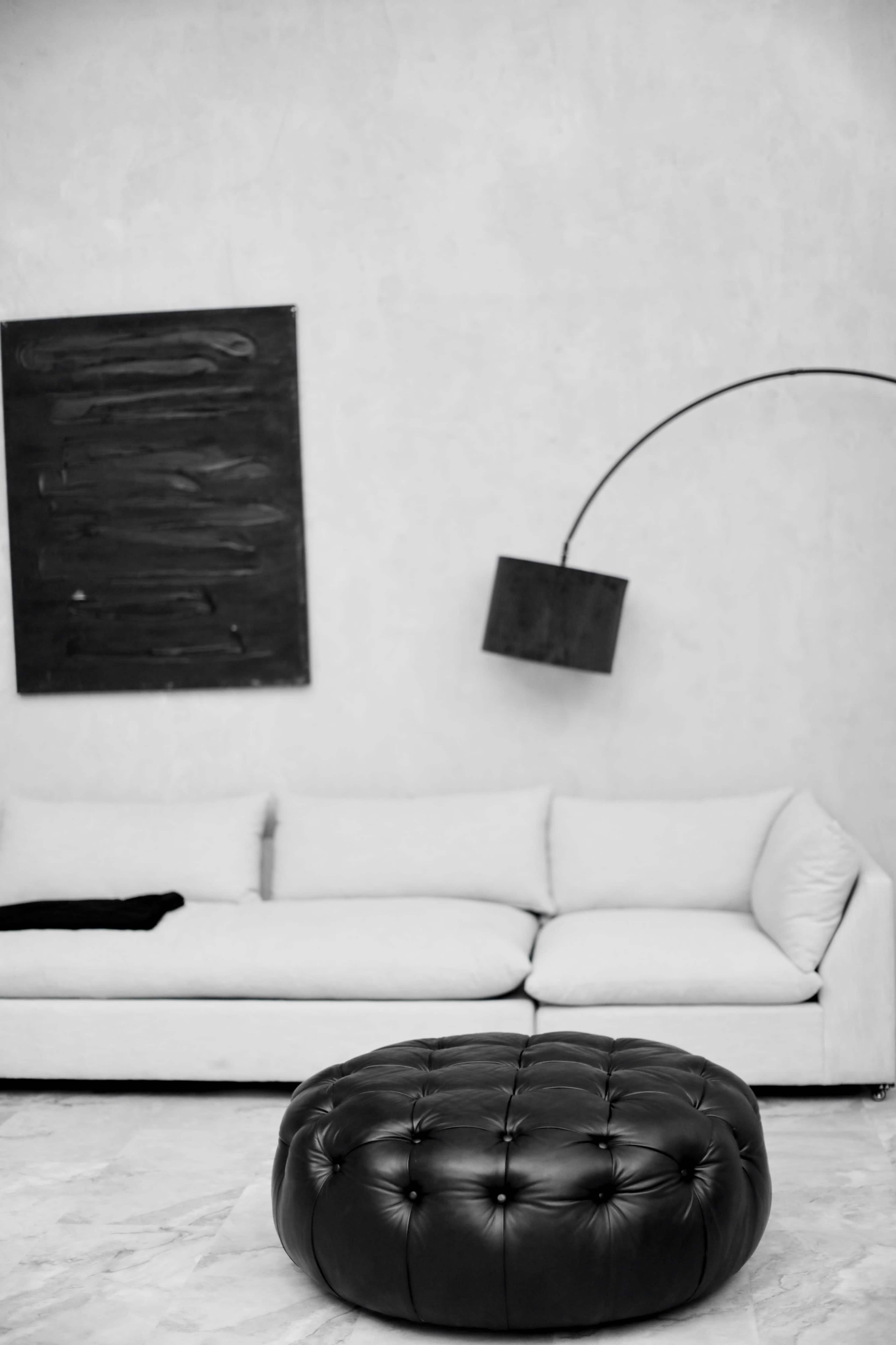 A modern living room features a white sofa, a black ottoman, and a minimalist wall lamp.