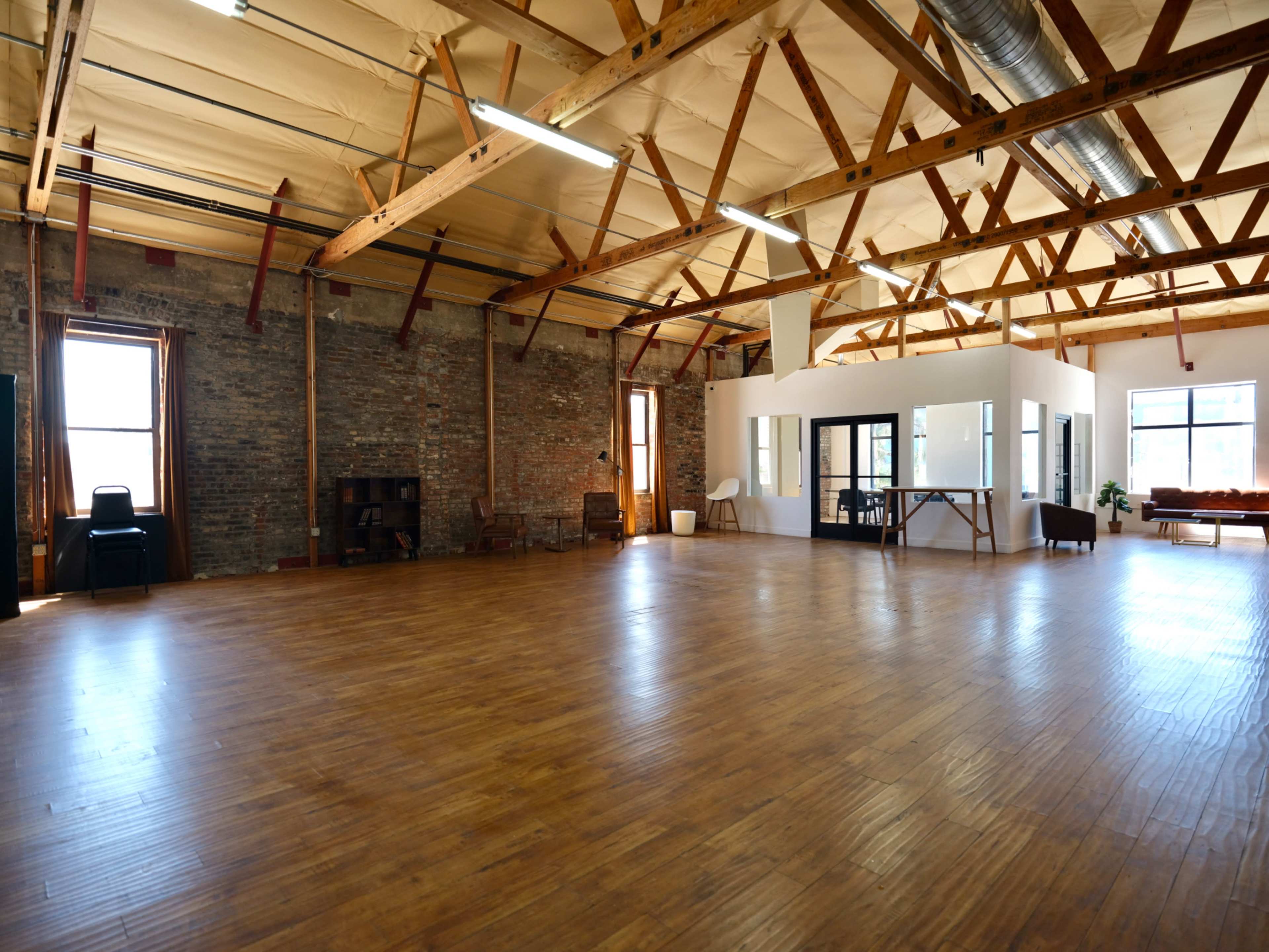 A spacious interior room with wooden floors, exposed brick walls, and high ceilings supported by wooden beams.