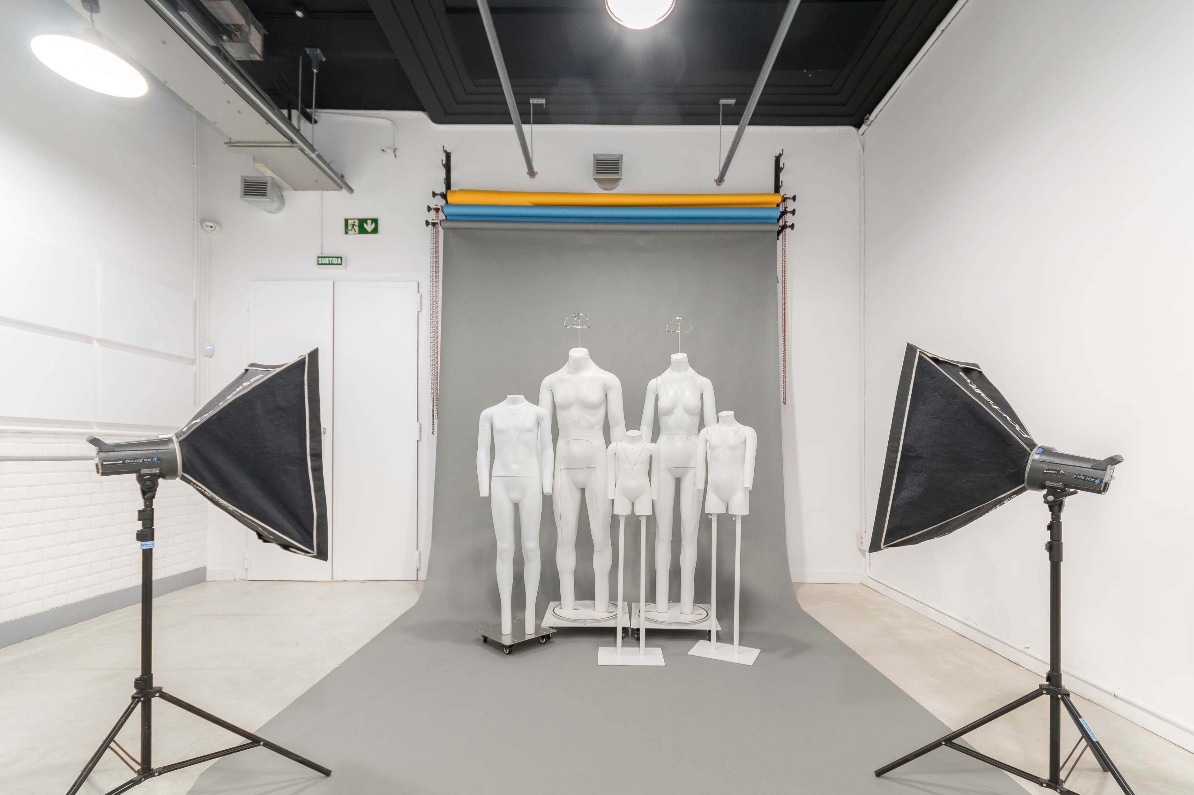 A photography studio setup with several mannequins positioned in front of a gray backdrop and two softbox lights on either side.