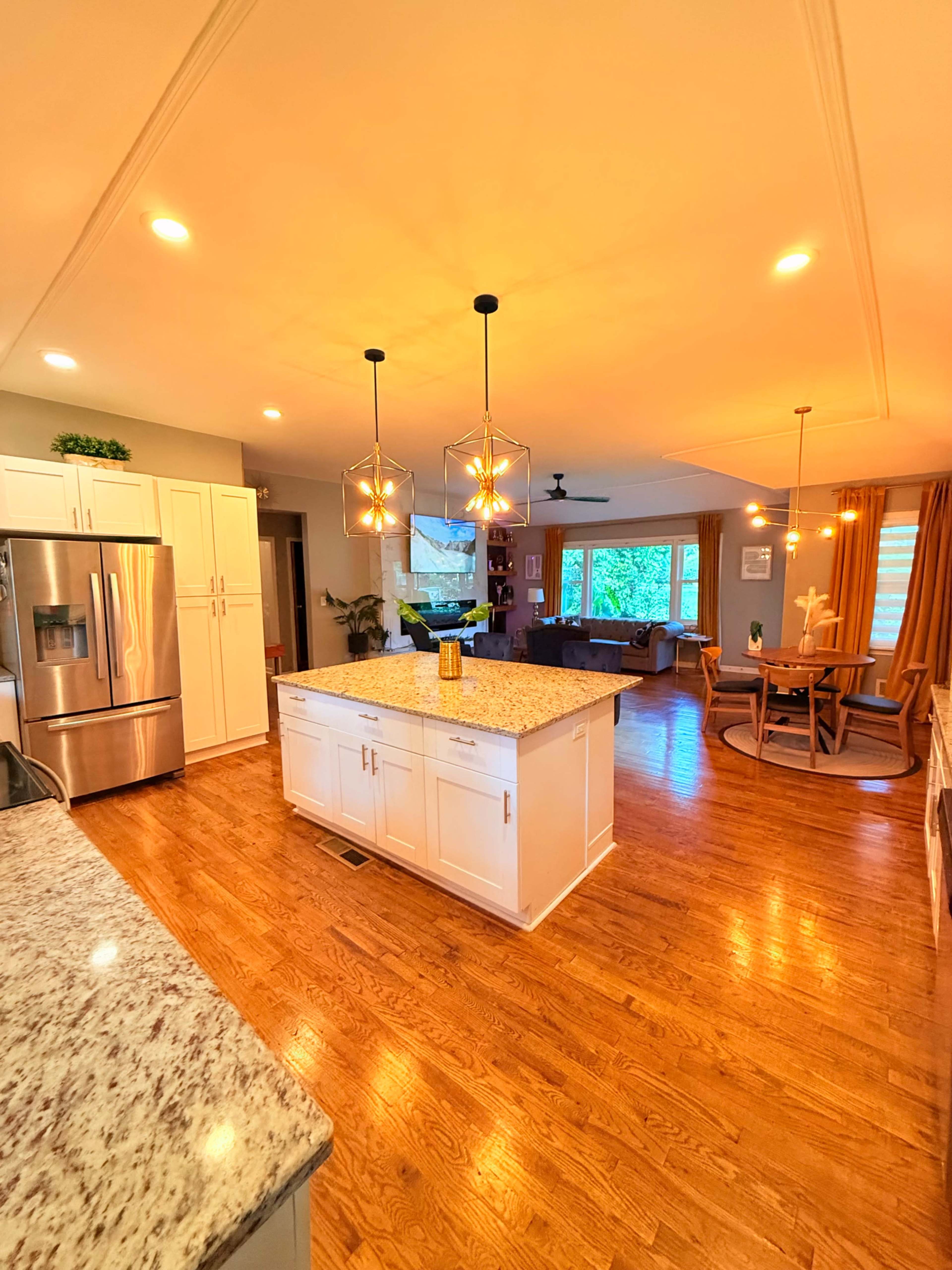 The kitchen features a large island with a granite countertop, stainless steel appliances, and pendant lighting, opening into a bright dining area and living space.