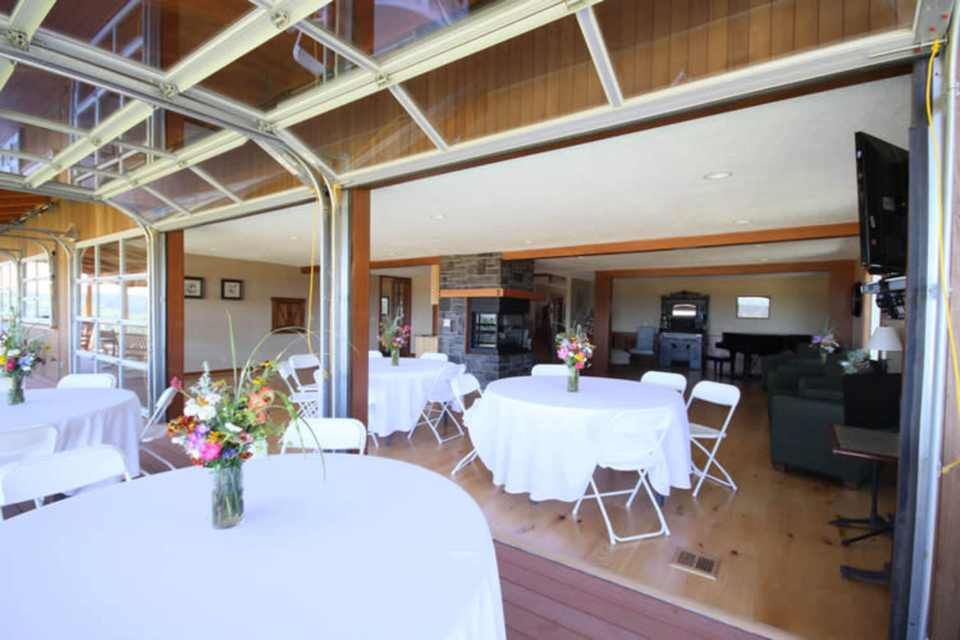 An indoor venue with tables set for an event, featuring large windows that open to an outdoor area.