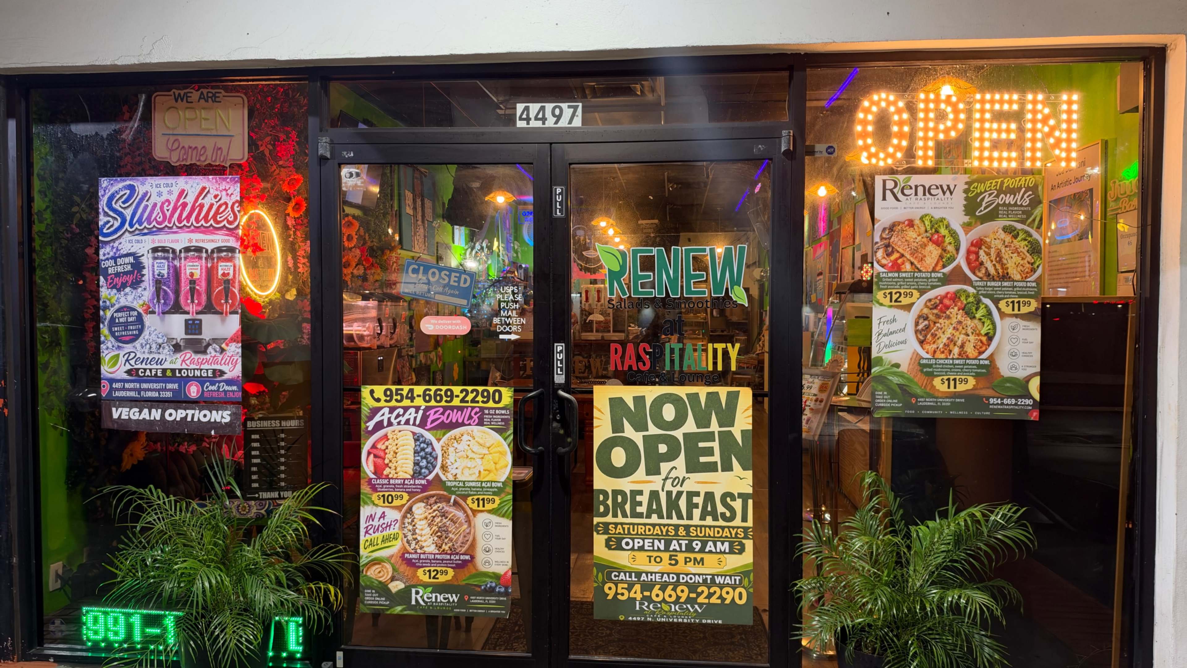 The entrance of a restaurant features a bright "OPEN" sign, multiple menu advertisements, and colorful decorations.