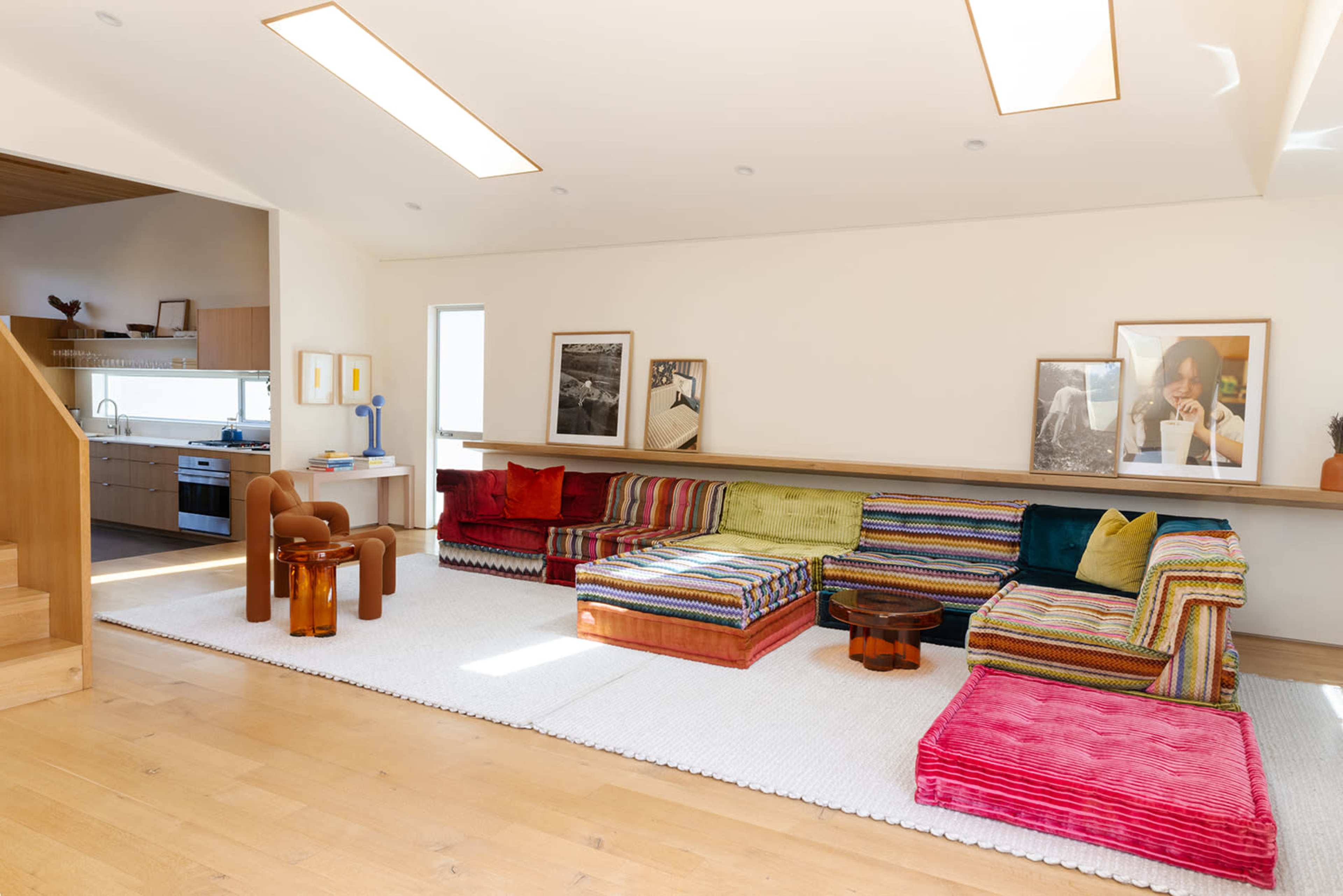 A colorful seating area features a multicolored sectional couch, a round coffee table, and large windows that let in natural light.