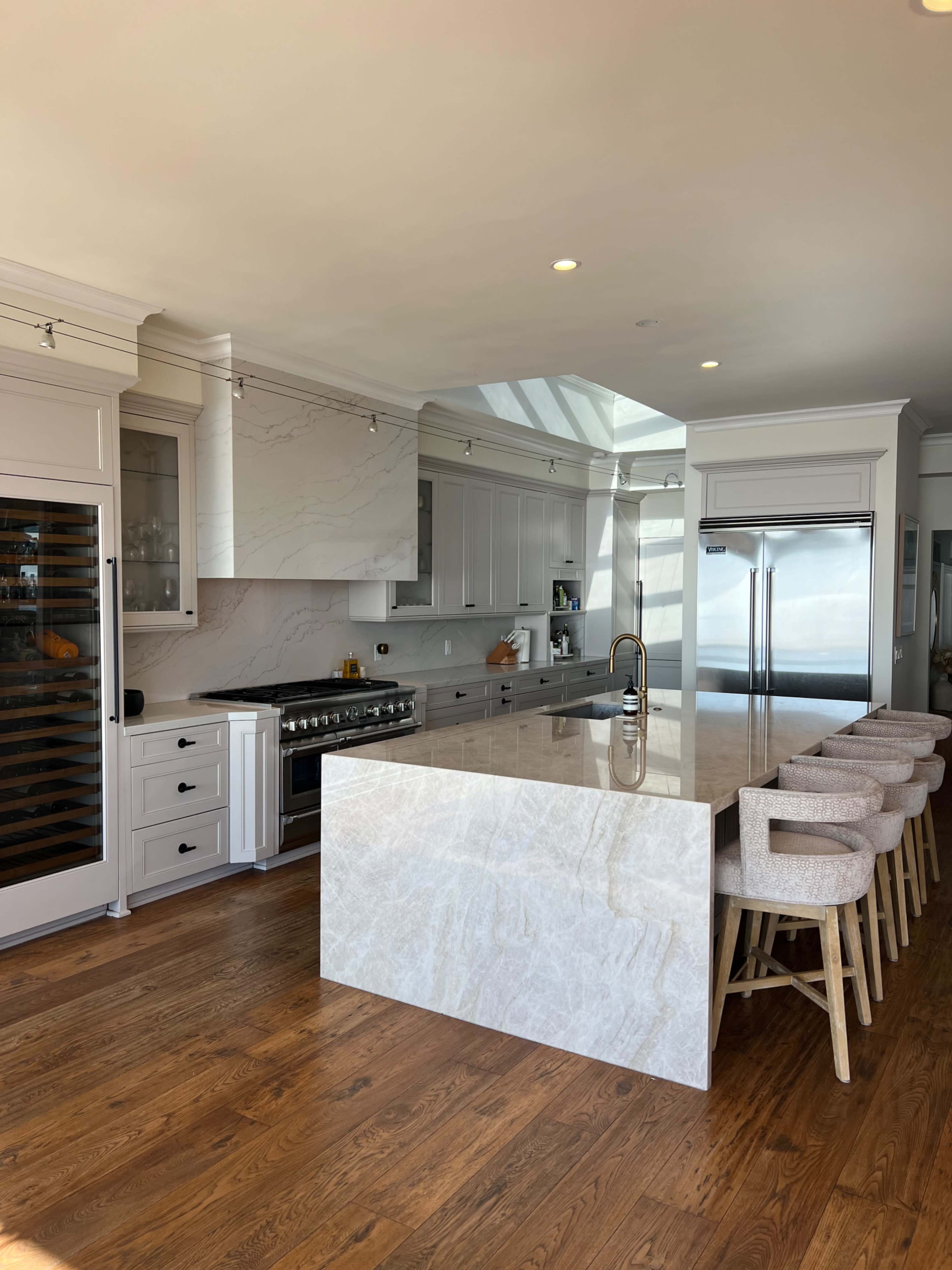 A modern kitchen featuring a large island with a marble countertop, white cabinetry, a stainless steel refrigerator, and bar stools arranged around the island.