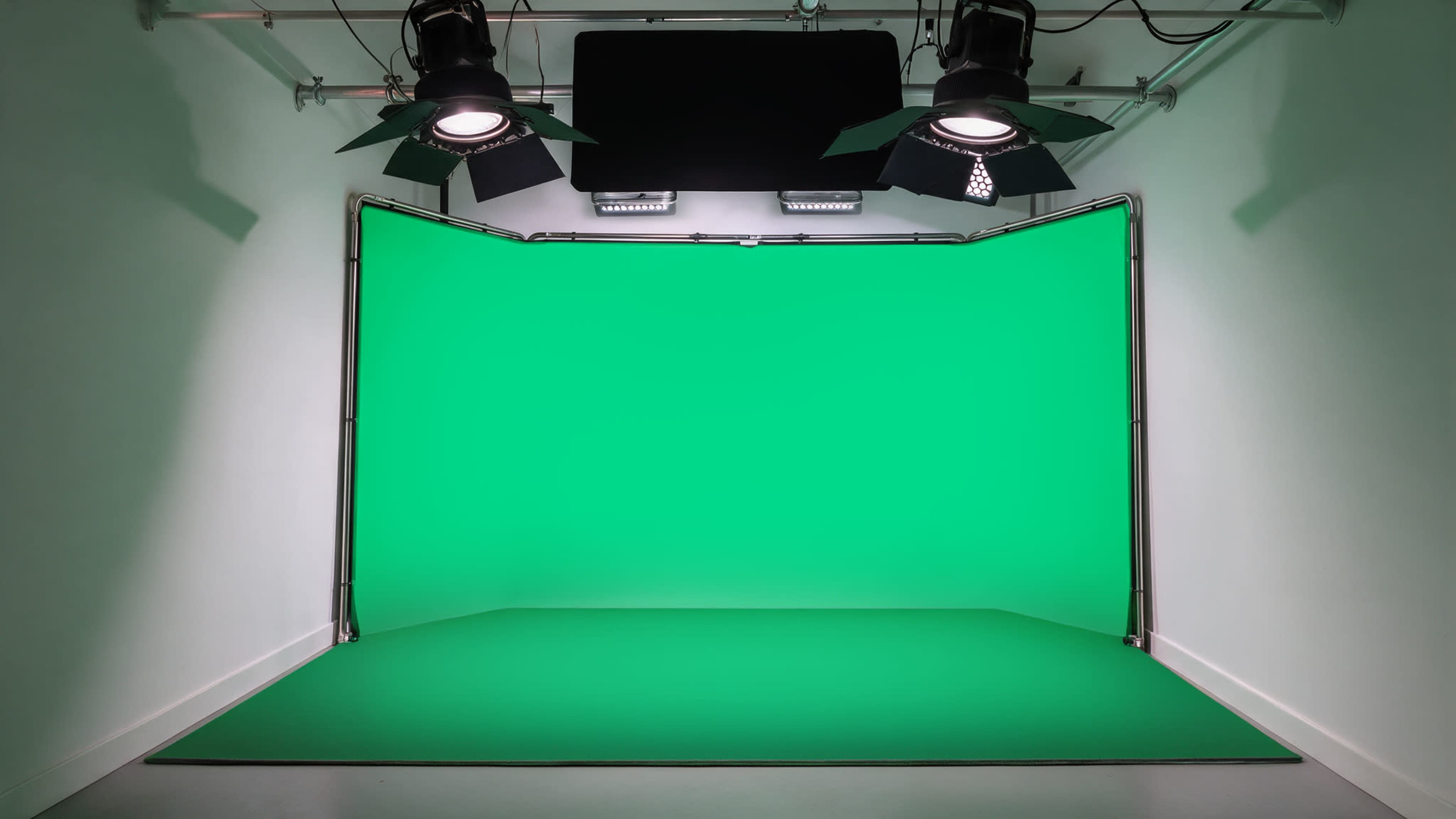 The image shows a green screen studio with overhead lights and a seamless green backdrop.
