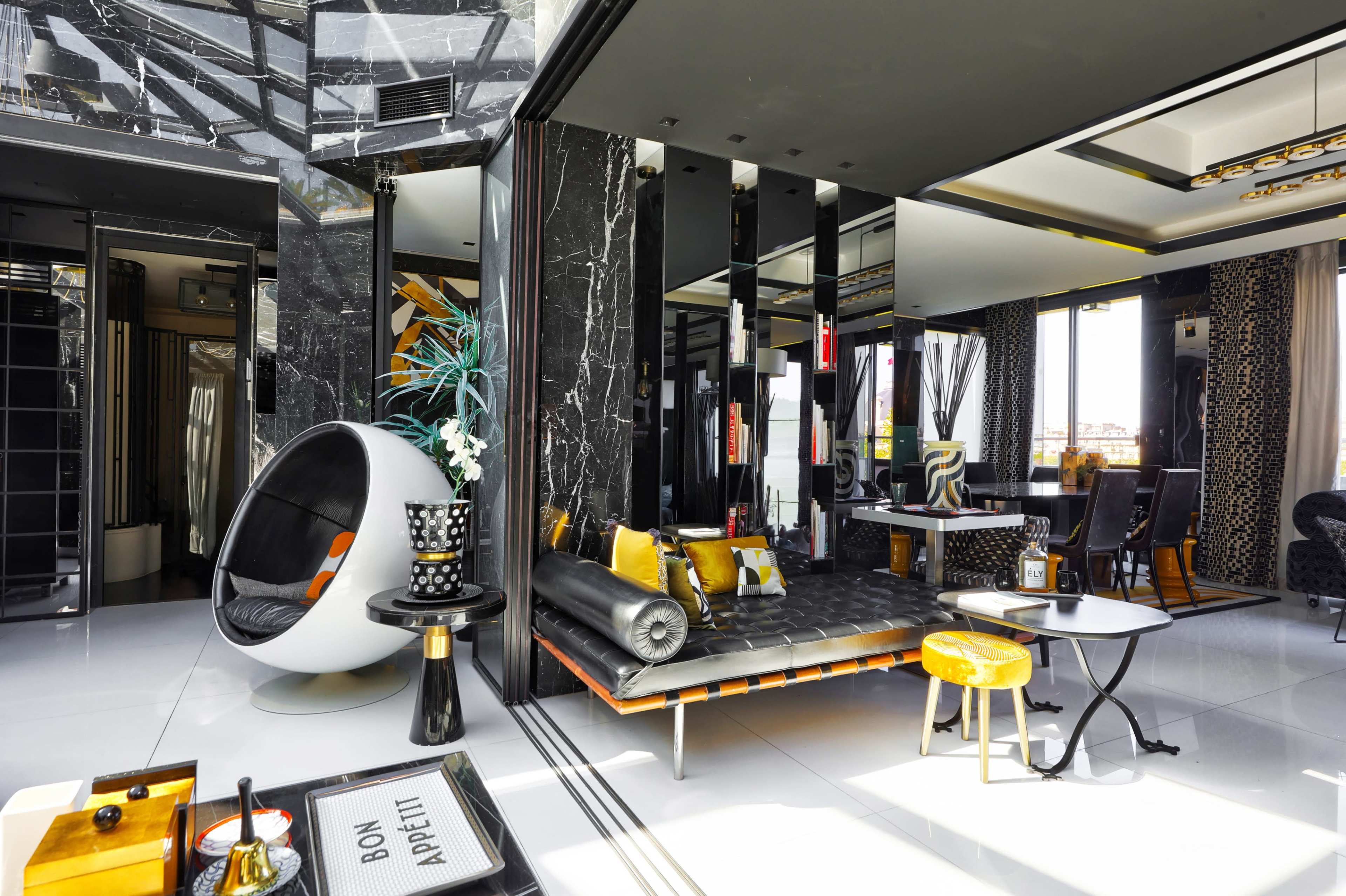 The image shows a modern interior space with sleek black and white design elements, featuring a circular chair, a minimalist black sofa, and decorative plants.