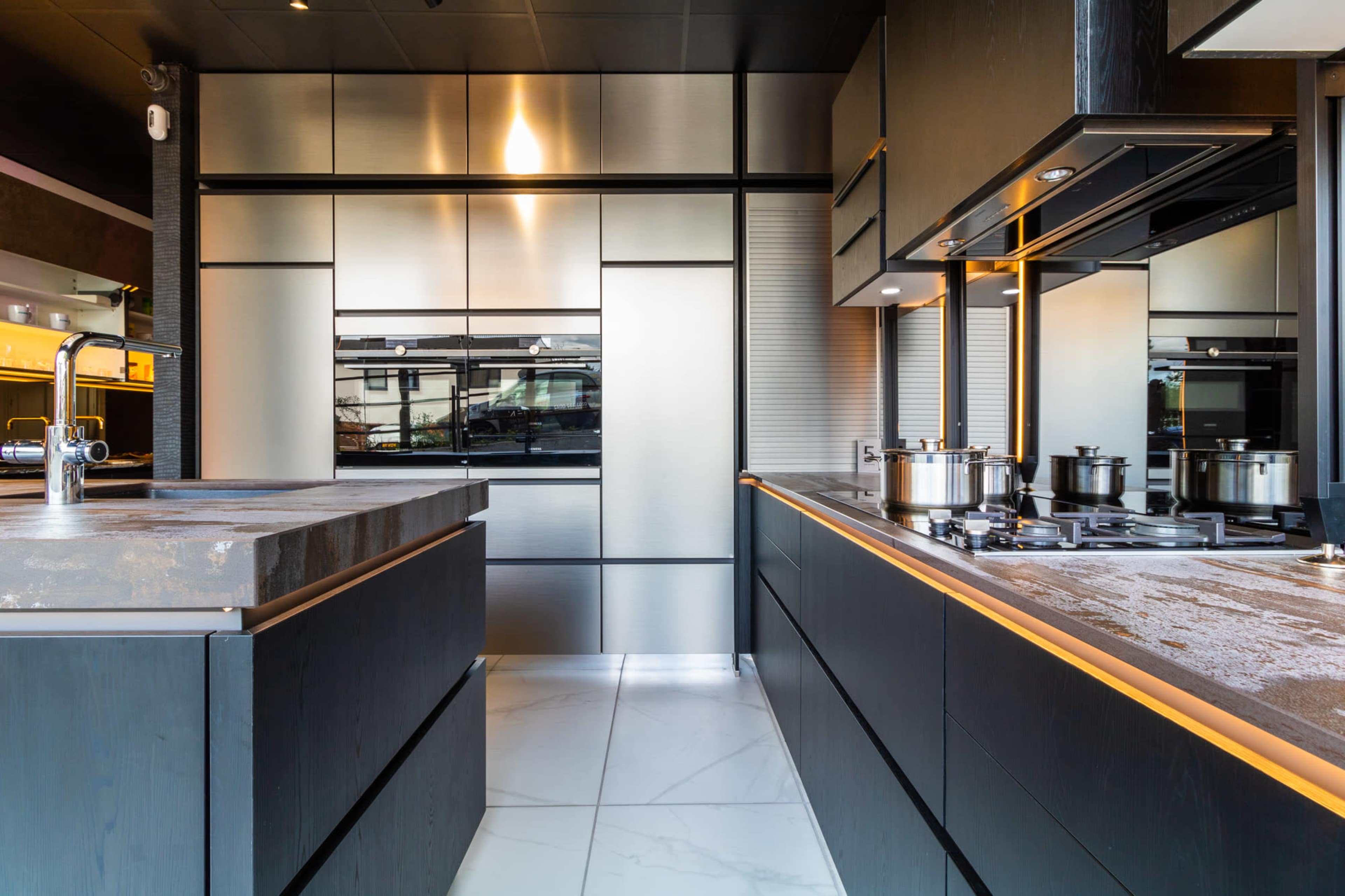 A modern kitchen with sleek, dark cabinetry, stainless steel appliances, and a contrasting light countertop.