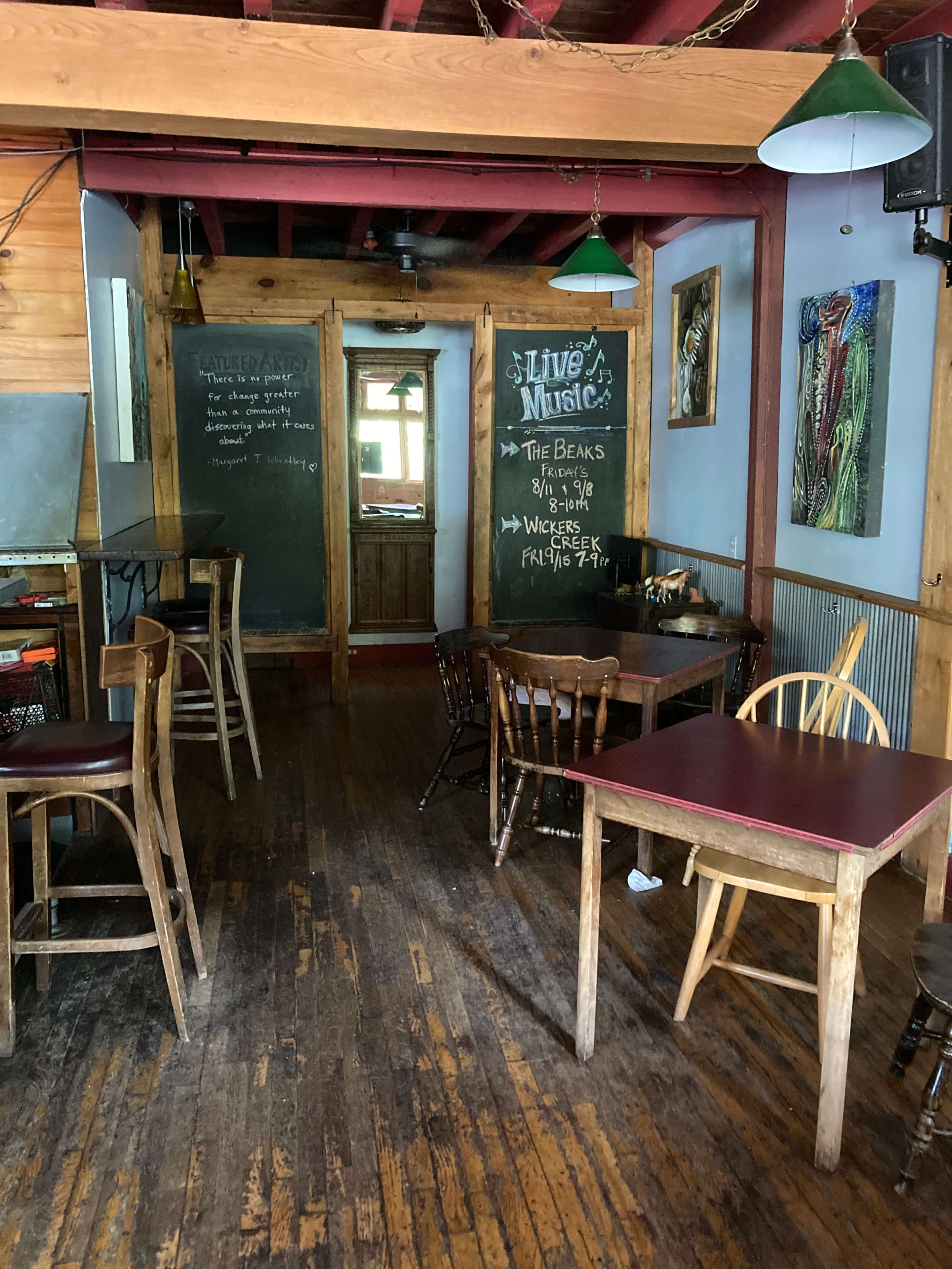 A wooden interior of a casual dining space with tables, chairs, and a chalkboard indicating live music events.