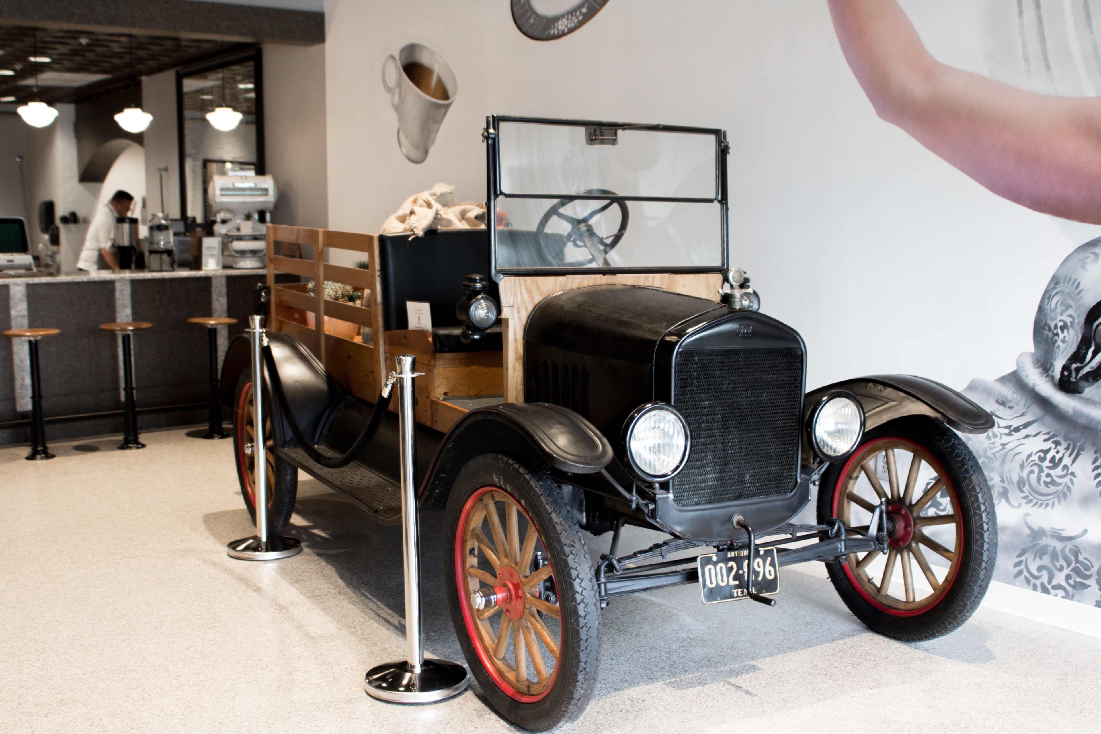 An antique black pickup truck with wooden sides is displayed inside a modern café.
