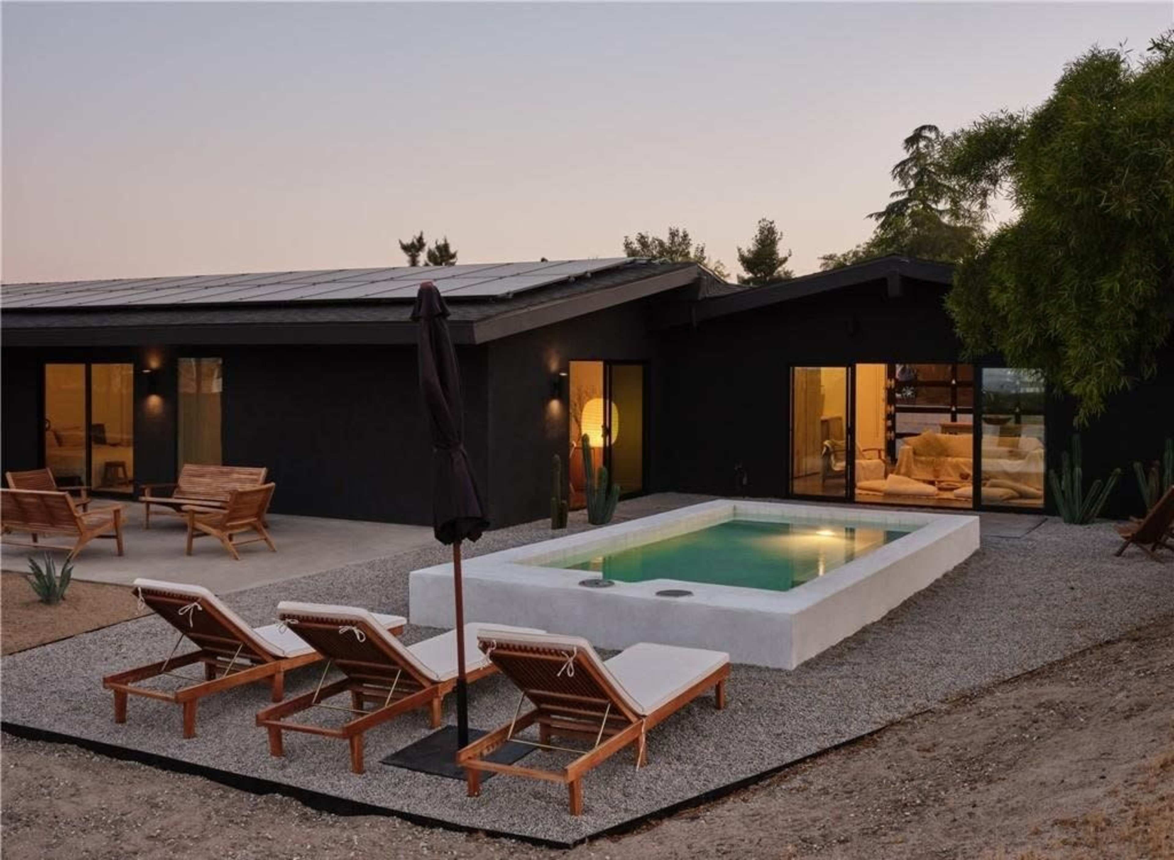 A modern house with a rectangular pool surrounded by lounge chairs on a gravel patio.