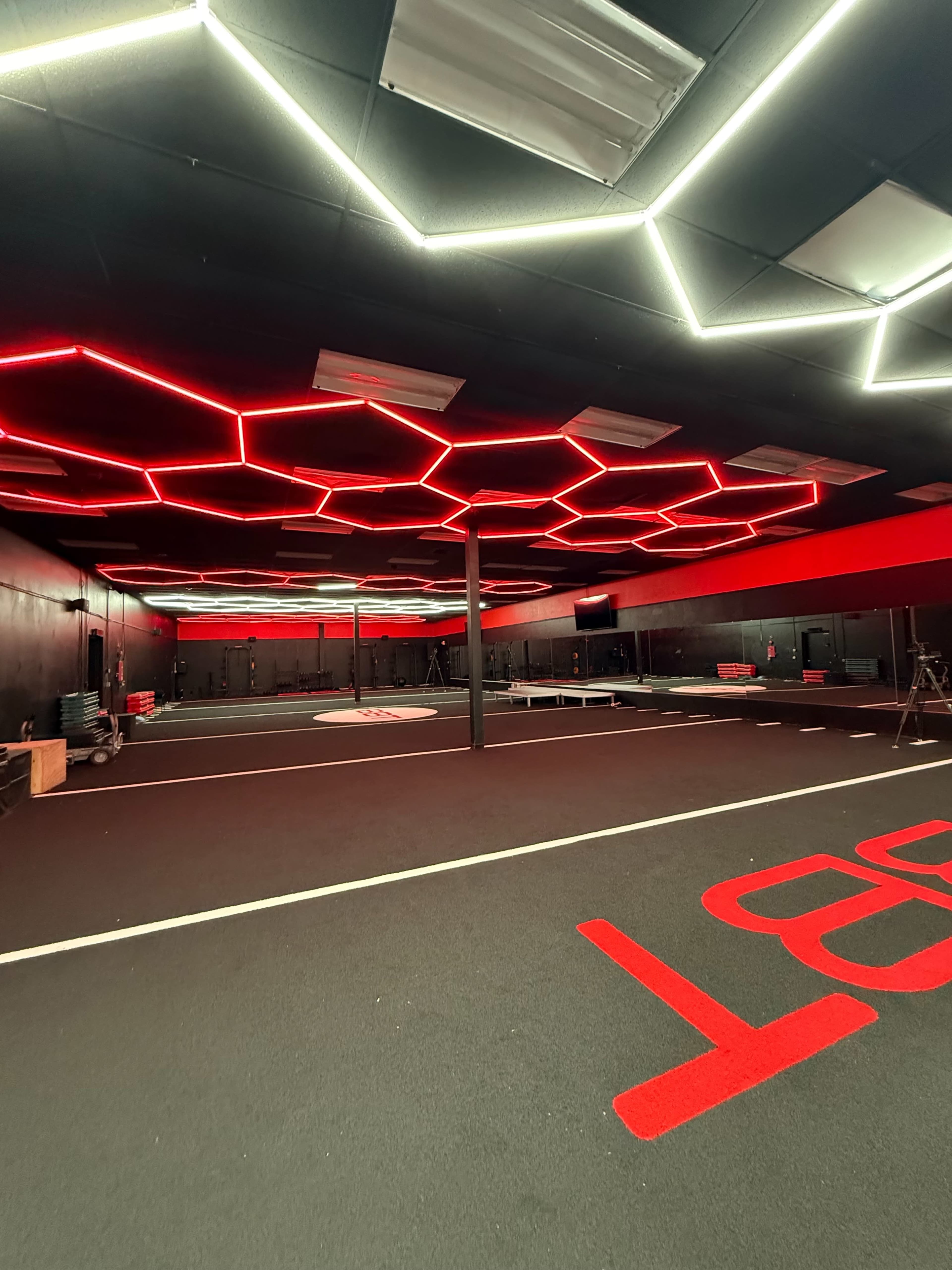 The image shows a fitness studio with a black and red color scheme, featuring hexagonal red LED lighting on the ceiling and exercise equipment visible in the background.