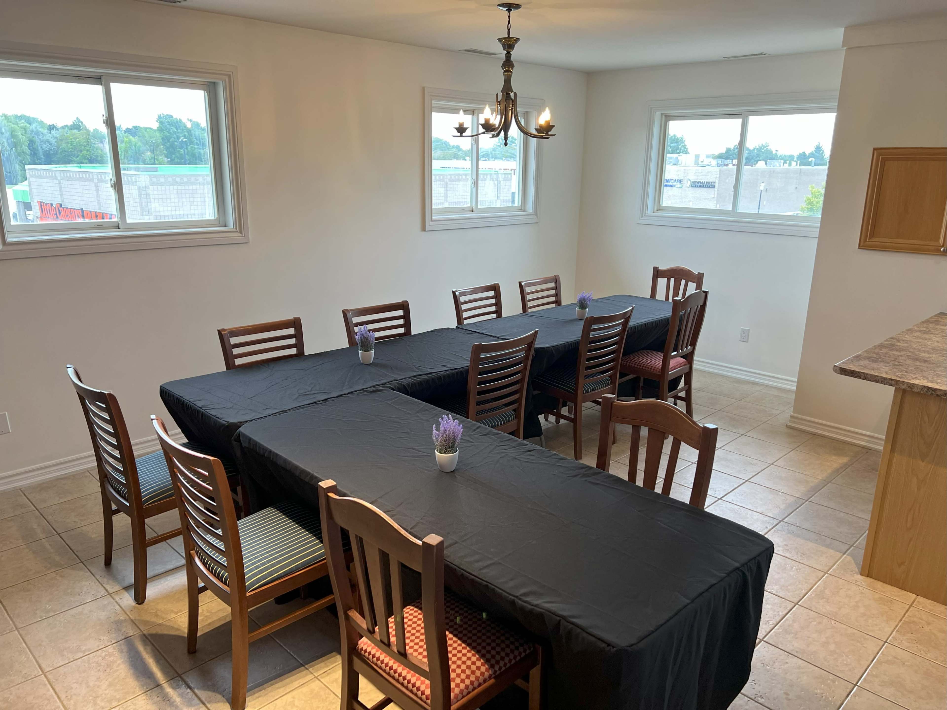 A dining room with two long tables covered in black tablecloths, surrounded by wooden chairs, and featuring a chandelier overhead.