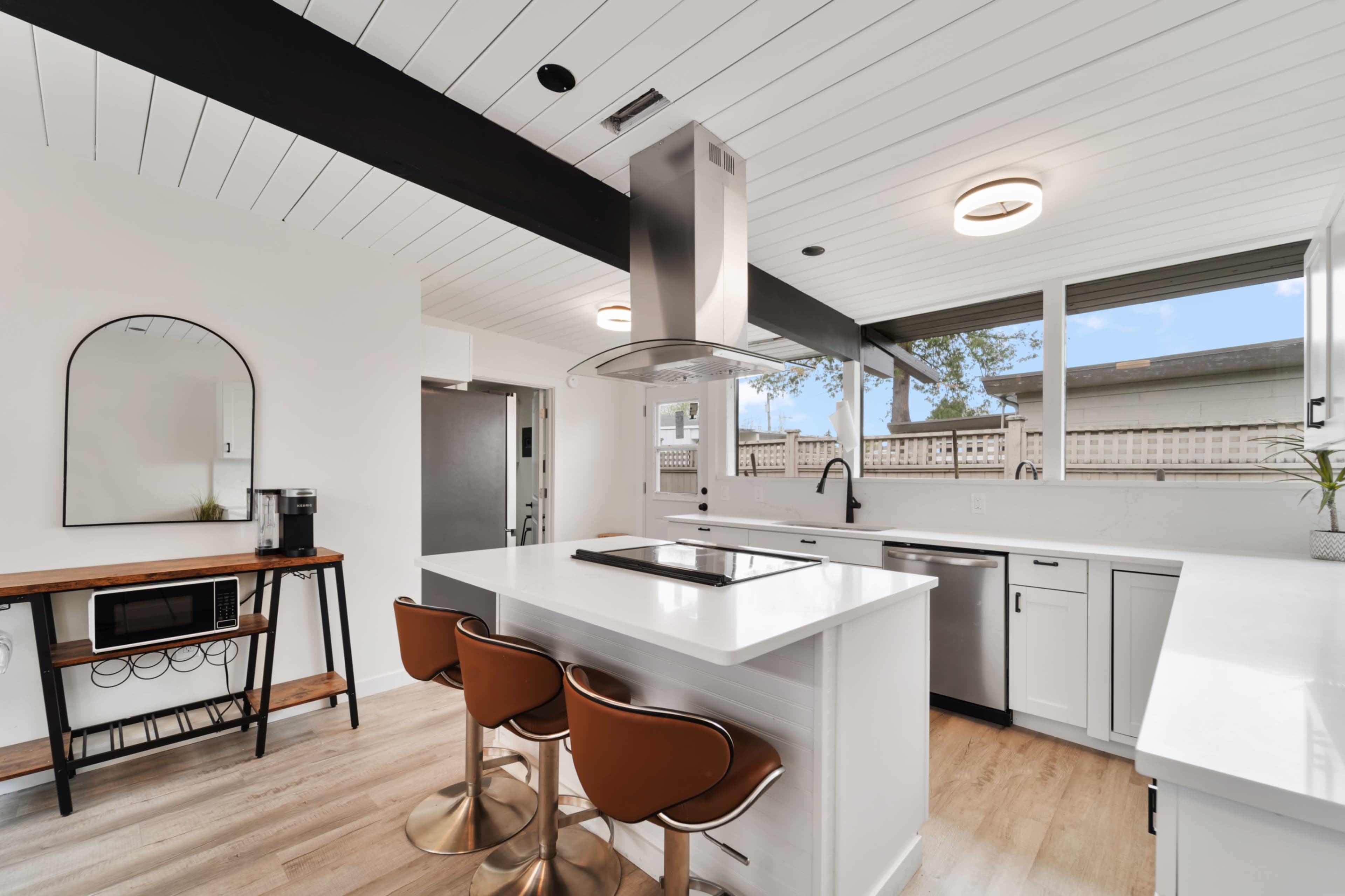 A modern kitchen with a central island, three brown bar stools, and large windows providing natural light.