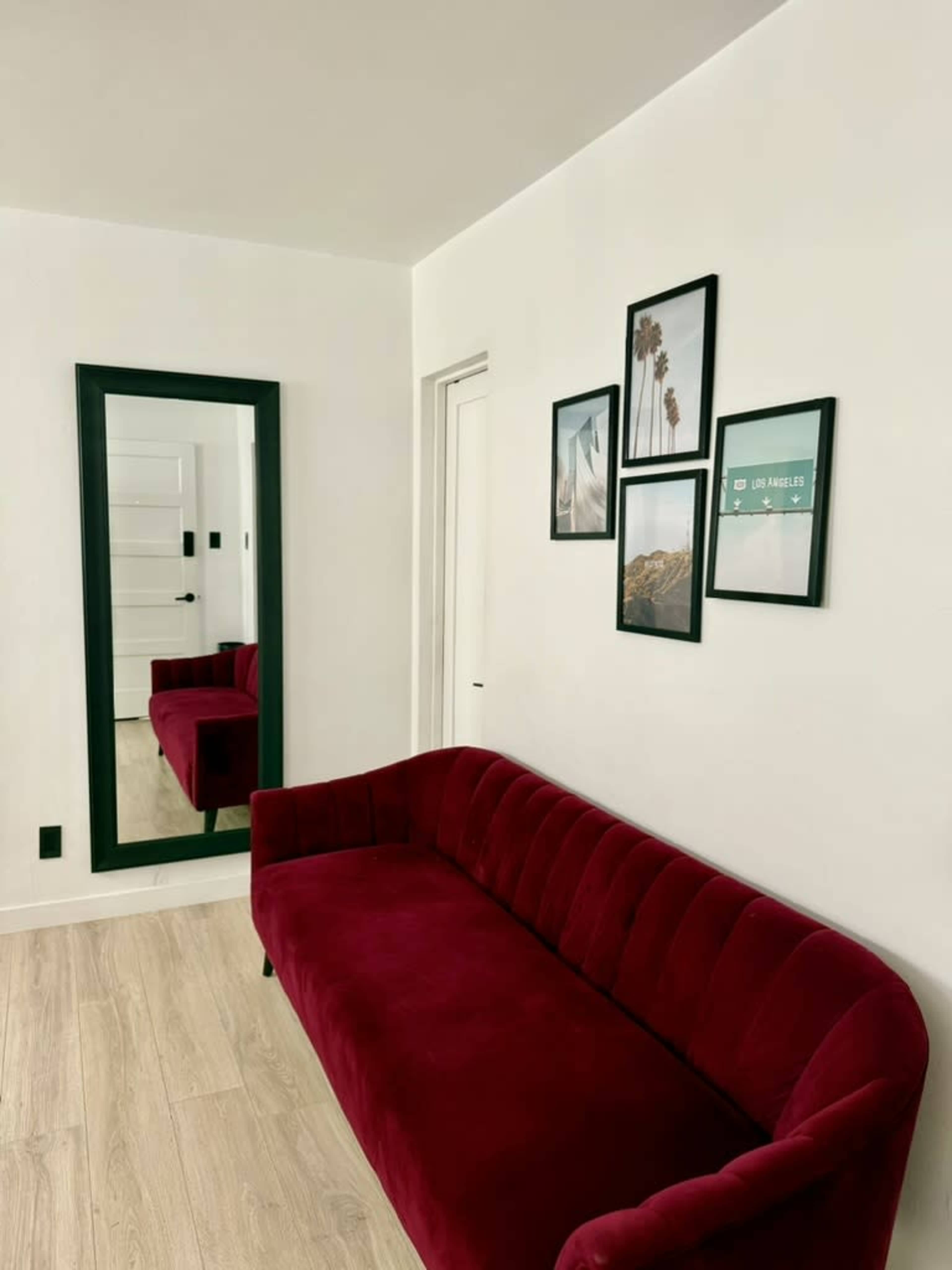 A red velvet couch sits in a well-lit room next to a large mirror and a gallery wall of framed photographs.