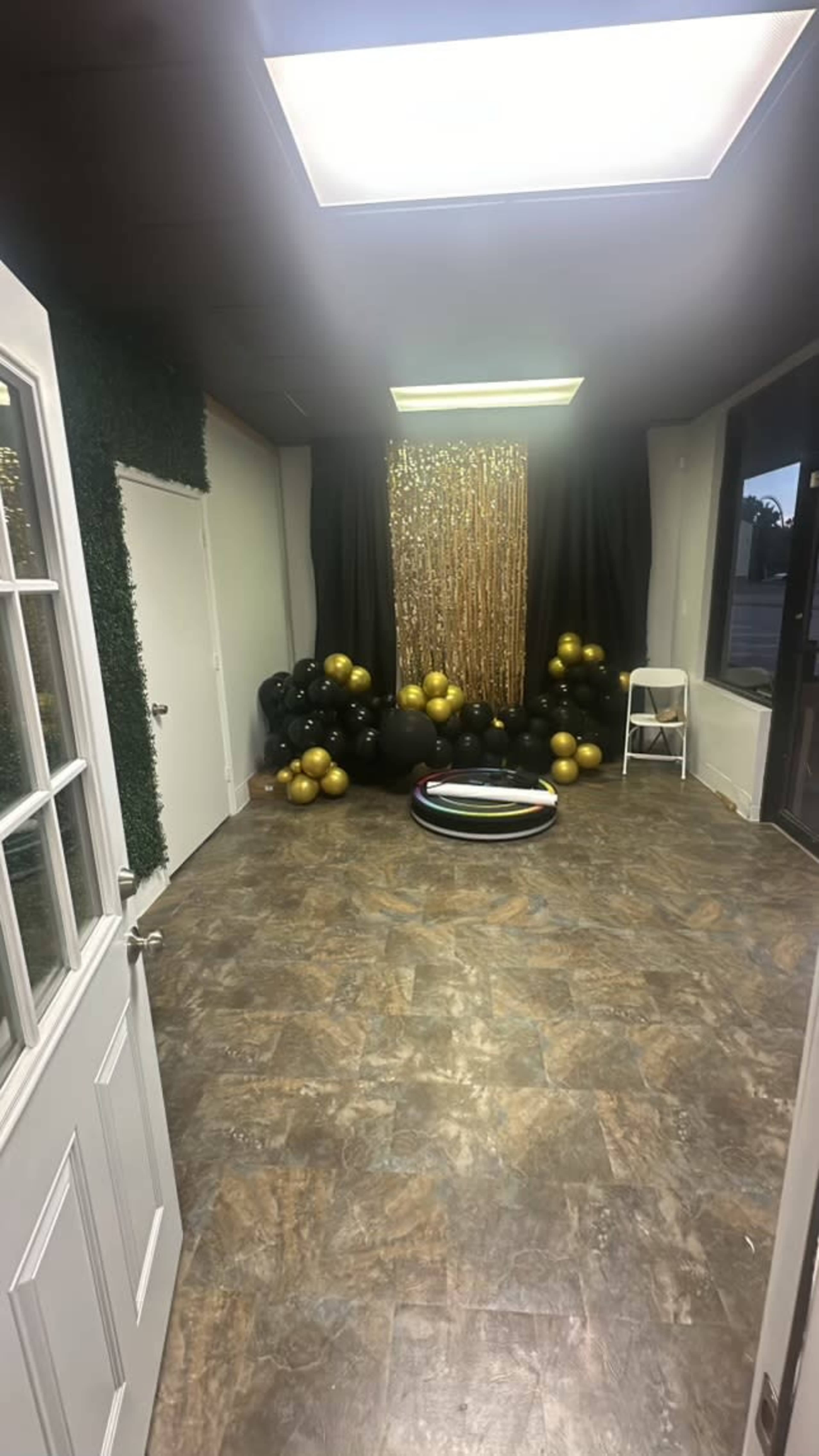 A decorated room with a backdrop of gold fringe and a cluster of black and gold balloons positioned to one side.
