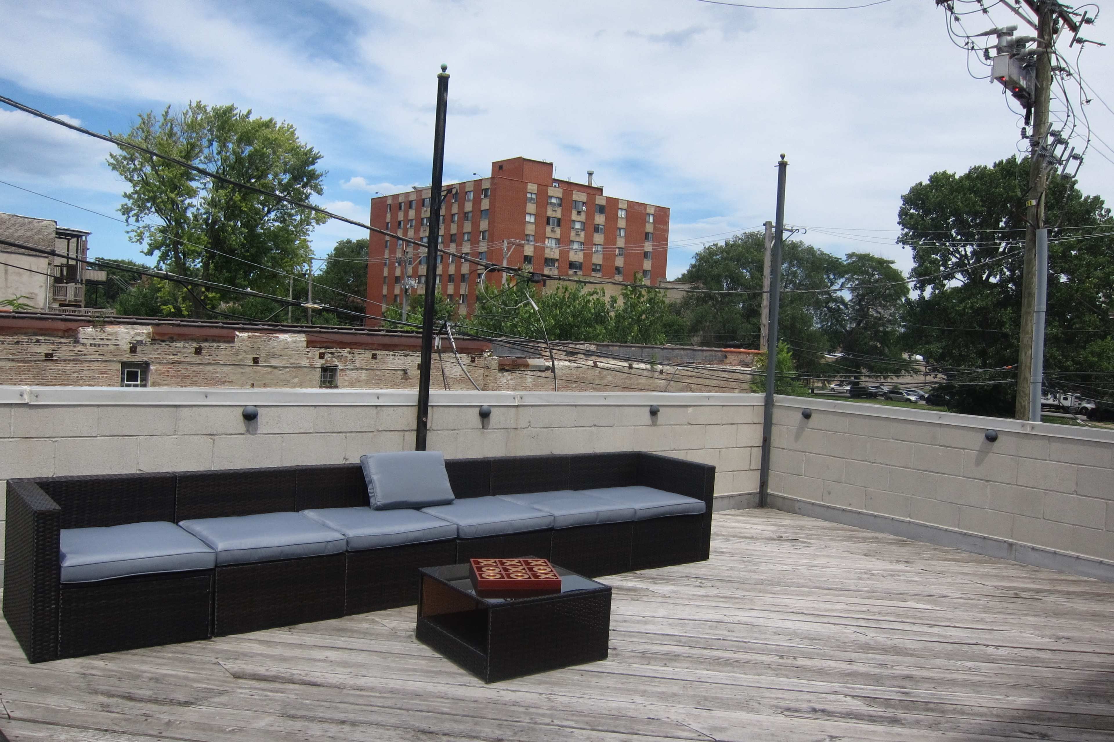 A rooftop area with a sectional couch and a small table made of wicker, surrounded by a concrete wall and power lines above.