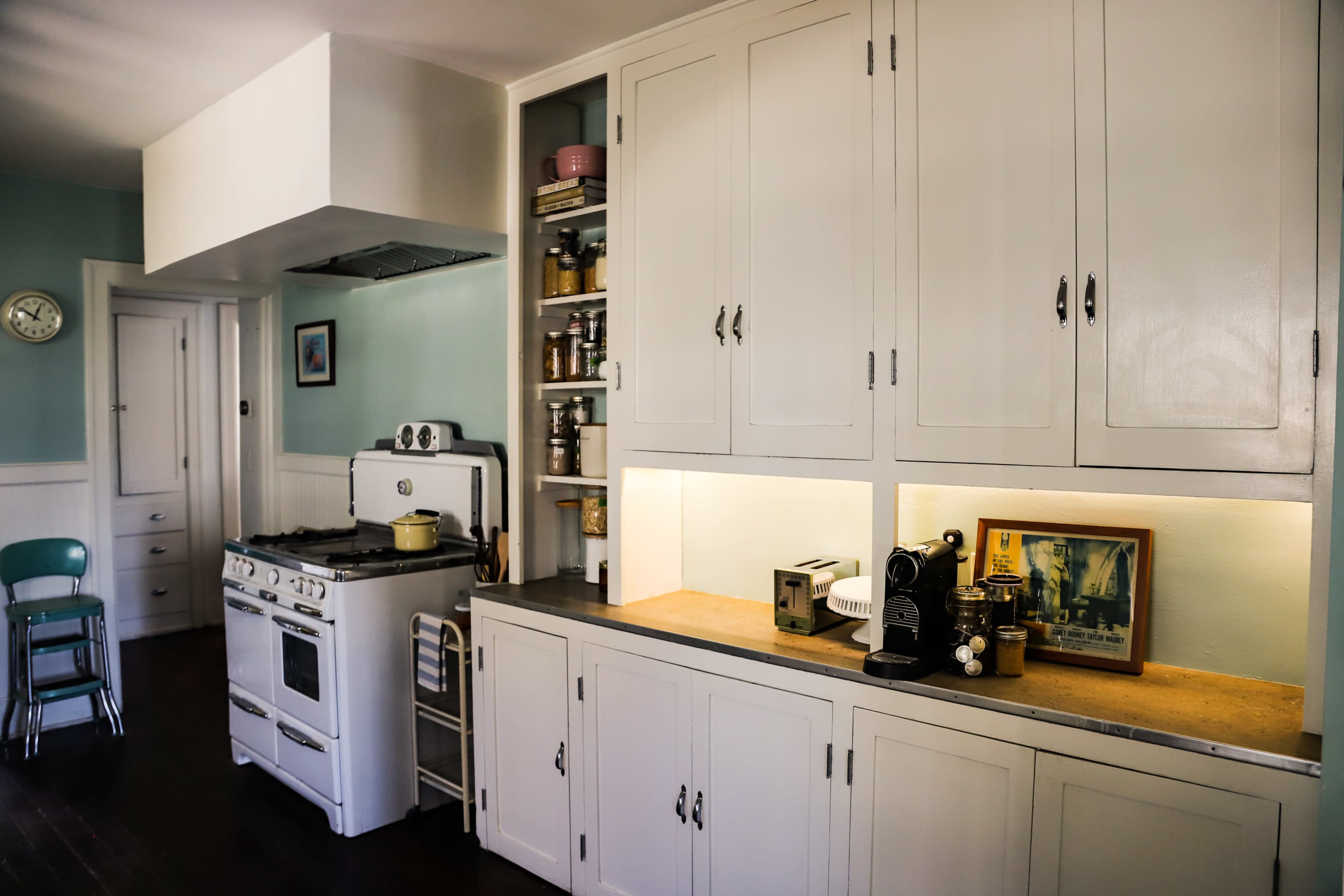 A kitchen features white cabinets, a vintage stove, and a countertop with various kitchen appliances and jars.