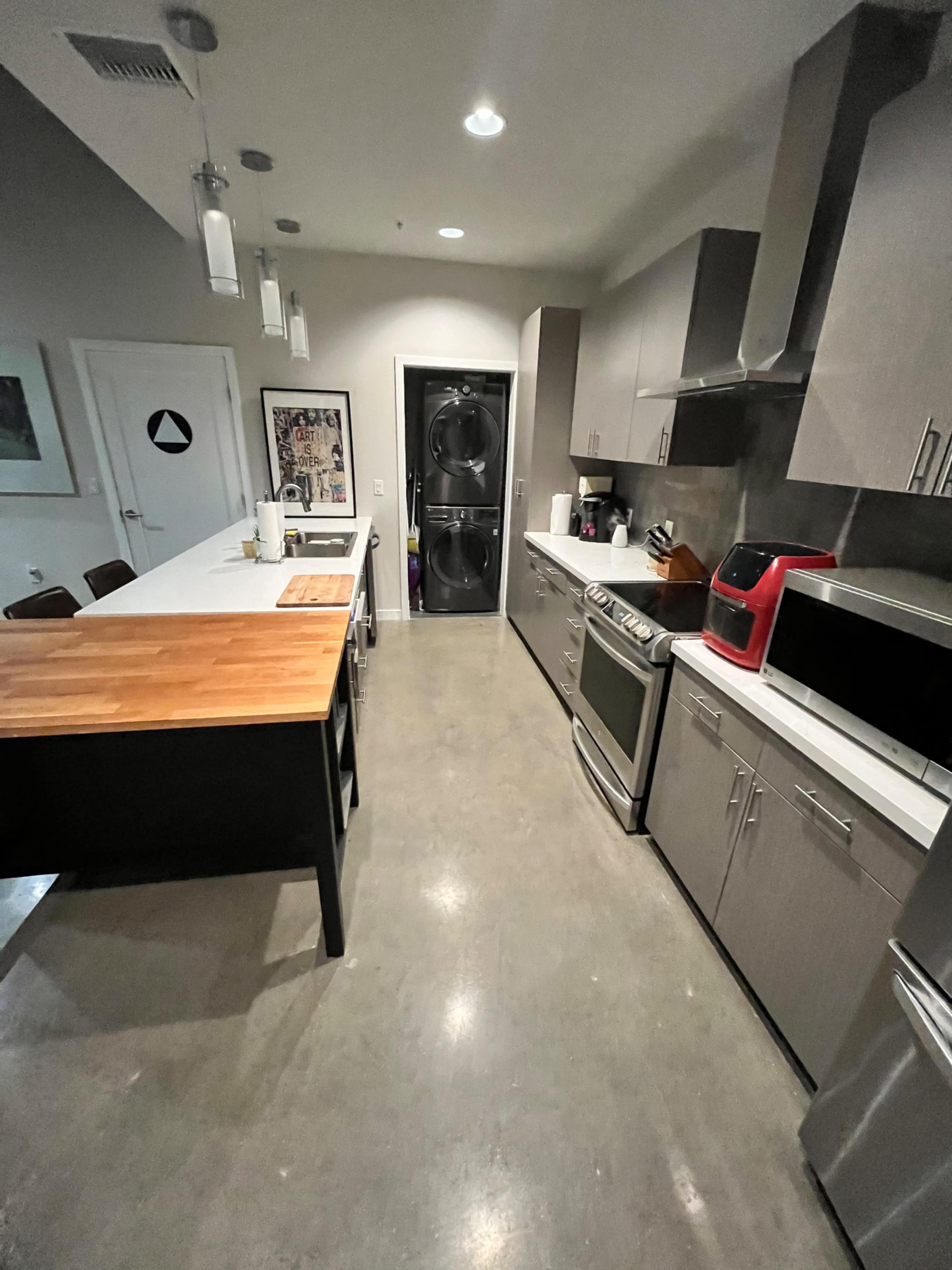 A modern kitchen features a central island with a wooden top, stainless steel appliances, and a laundry area with a stacked washer and dryer behind a door.