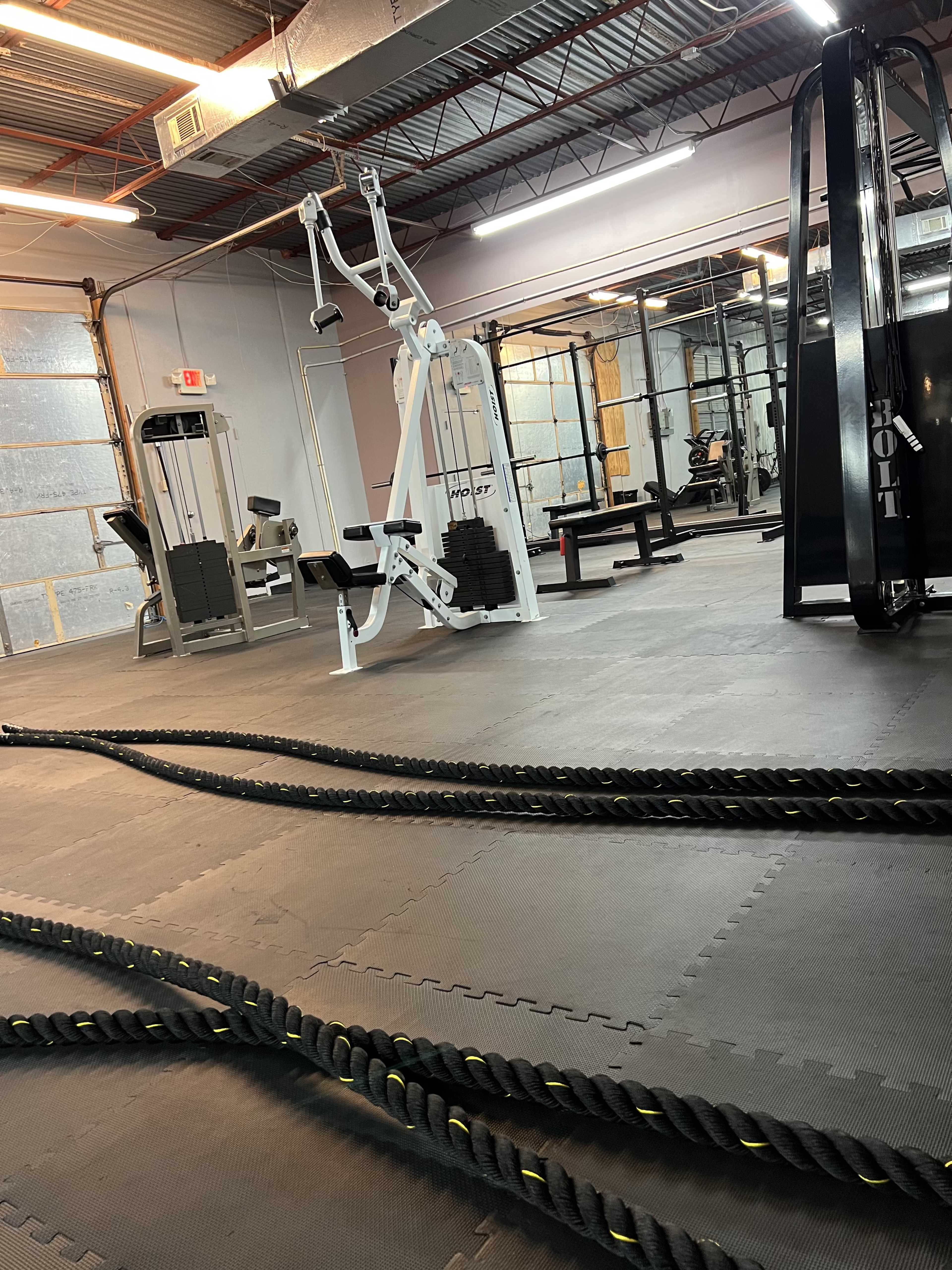 A spacious gym with various exercise equipment, including weight machines and battle ropes on the floor.