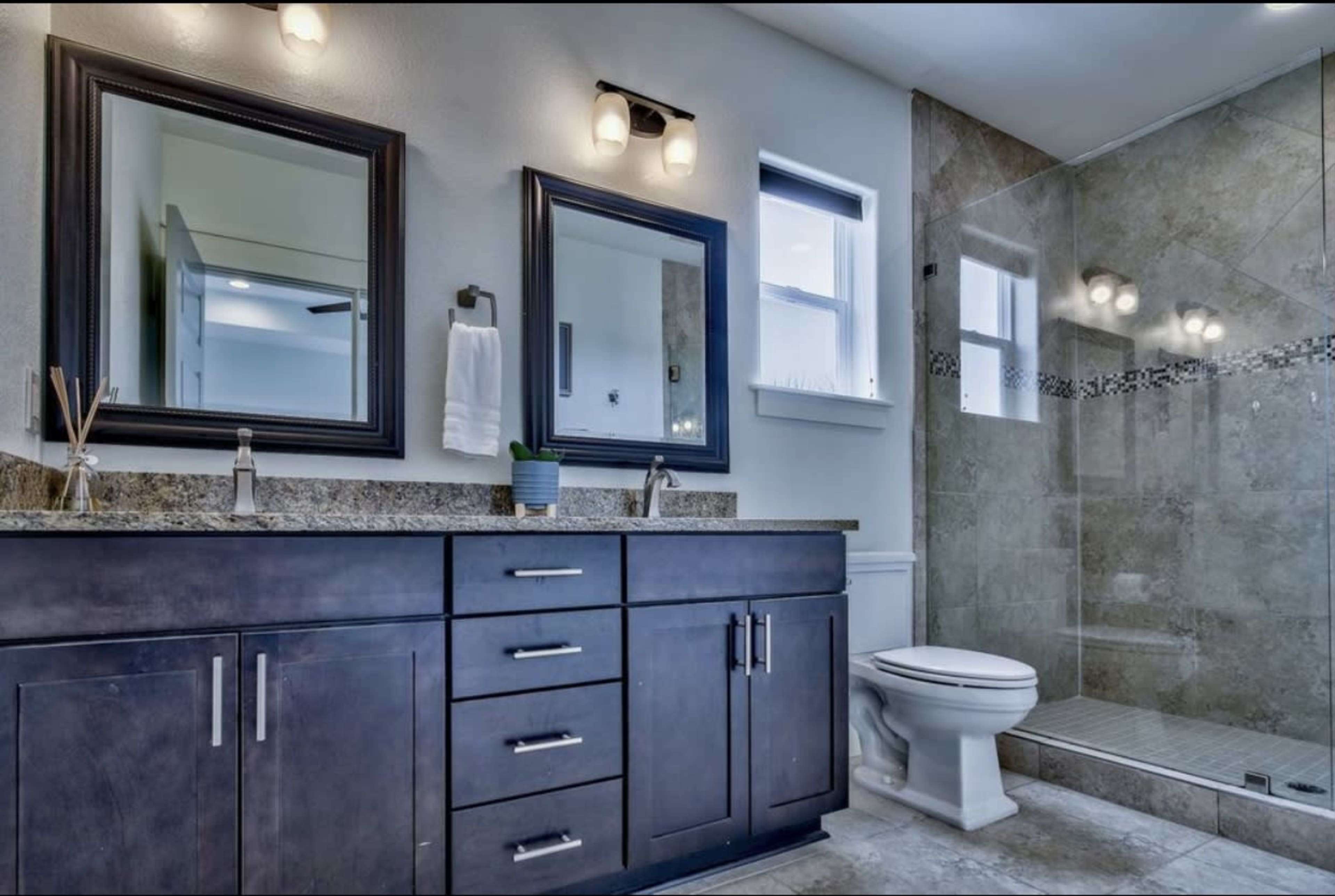 A modern bathroom features a double sink vanity with dark cabinets, two framed mirrors, a glass shower enclosure, and tiled walls.